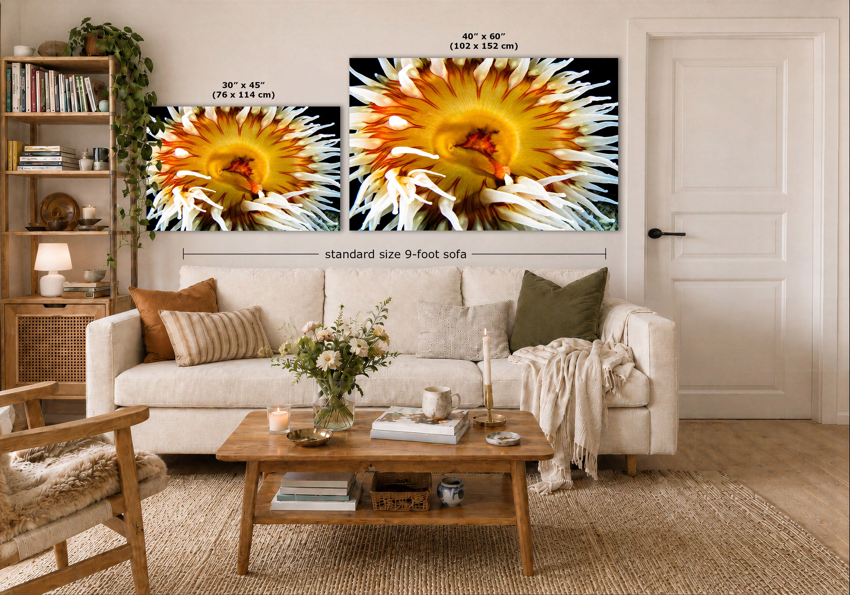 A styled living room showing two large framed wall art prints above a white sofa, with size labels indicating 30 x 45 inches and 40 x 60 inches. The room includes a wooden coffee table, rug, bookshelf, and door in a bright, real interior setting.