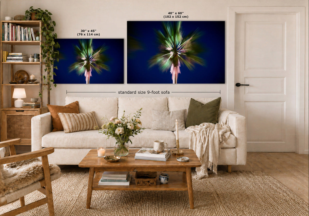A styled living room showing two wall art prints above a white sofa. The prints depict a colorful abstract floral or palm-like design on a deep blue background.