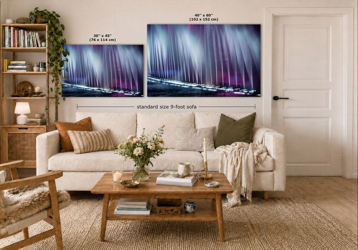 A styled living room showing two abstract fountain wall art prints above a white sofa. The prints depict a dramatic purple and blue abstract water scene.