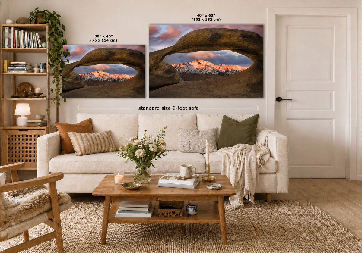 Two wall art prints depicting desert arches over mountain sunsets are displayed above a white sofa in a styled living room. The image includes size callouts for the prints: 30 x 45 inches and 48 x 60 inches, with a note for a standard size 9-foot sofa.
