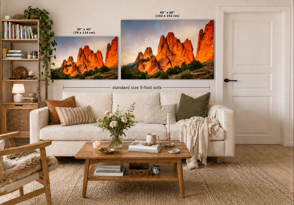 Two landscape wall art prints showing orange-red rock formations at sunset, displayed above a white sofa in a styled living room. Black text labels indicate the smaller print is 30 x 45 cm and the larger print is 40 x 60 cm, with a note for a standard size 9-foot sofa.