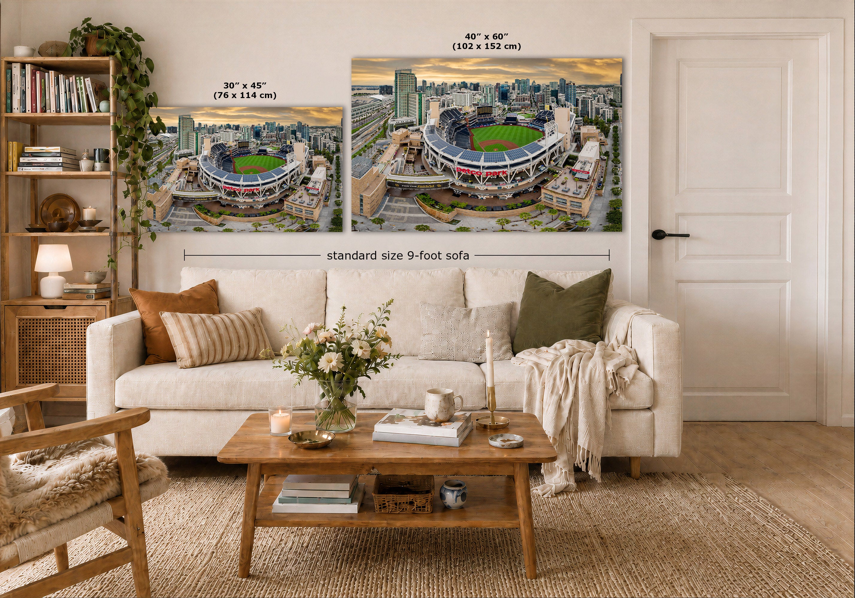 Two large wall art prints showing stadium cityscapes are displayed above a white sofa in a styled living room. The prints include size callouts and a dimension line reading standard size 9-foot sofa.