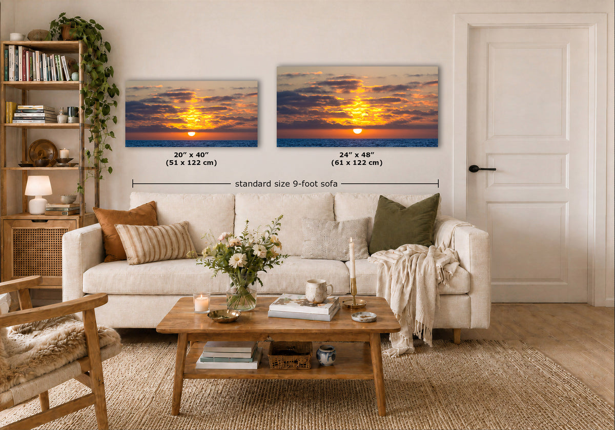 Two framed sunset wall art prints displayed above a white sofa in a bright living room. The left print is labeled 20" x 40" (51 x 122 cm) and the right print is labeled 24" x 48" (61 x 122 cm), with a dimension line reading standard size 9-foot sofa.