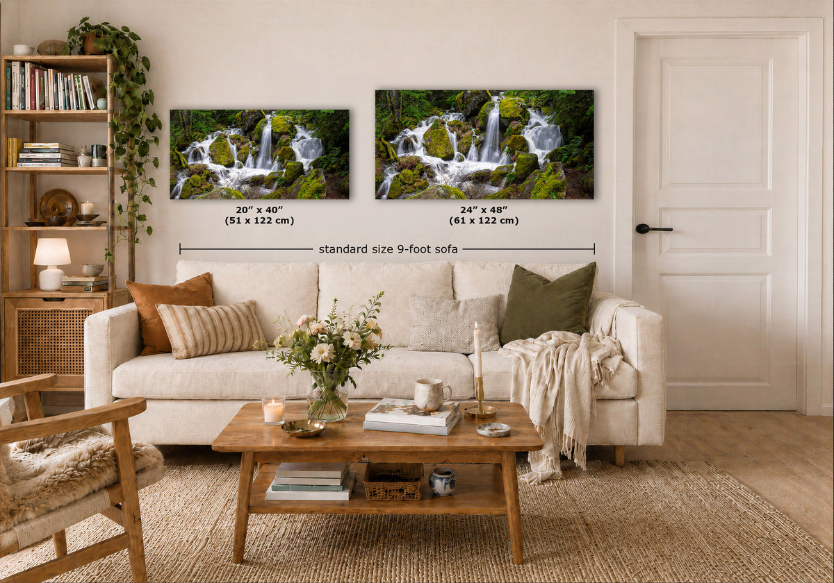 Two framed wall art prints showing waterfall scenes in a bright living room. The prints are mounted above a white sofa, with size labels overlaid: 20 x 40 in (51 x 122 cm) and 24 x 48 in (61 x 122 cm), plus a dimension line reading standard size 9-foot sofa.