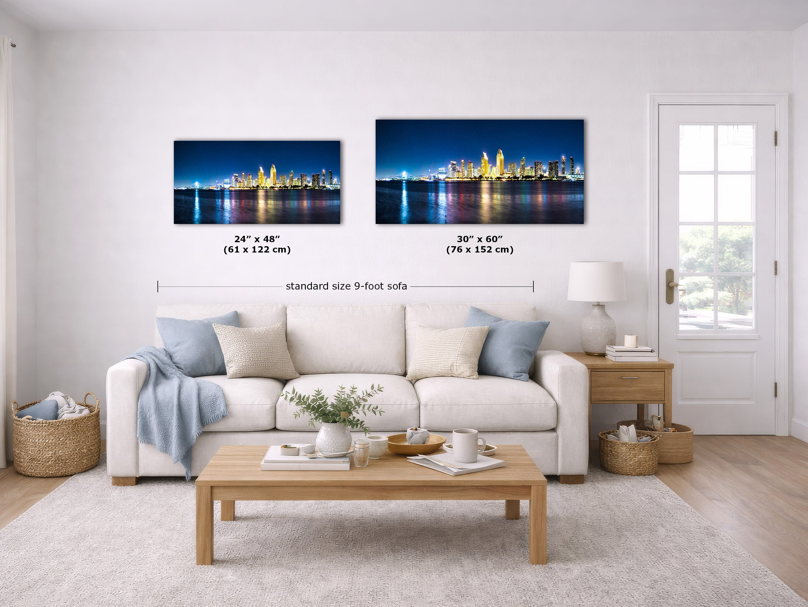A staged living room shows two framed city skyline wall art prints above a white sofa. The left print is labeled 24 x 48 inches (61 x 122 cm) and the right print is labeled 30 x 60 inches (76 x 152 cm), with text reading standard size 9-foot sofa.