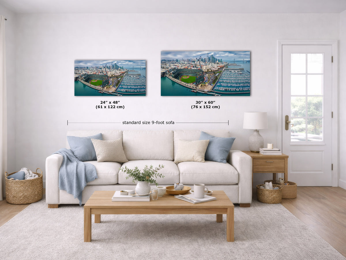 A staged living room shows two wall art prints above a white sofa. The prints depict an aerial harbor and cityscape scene.