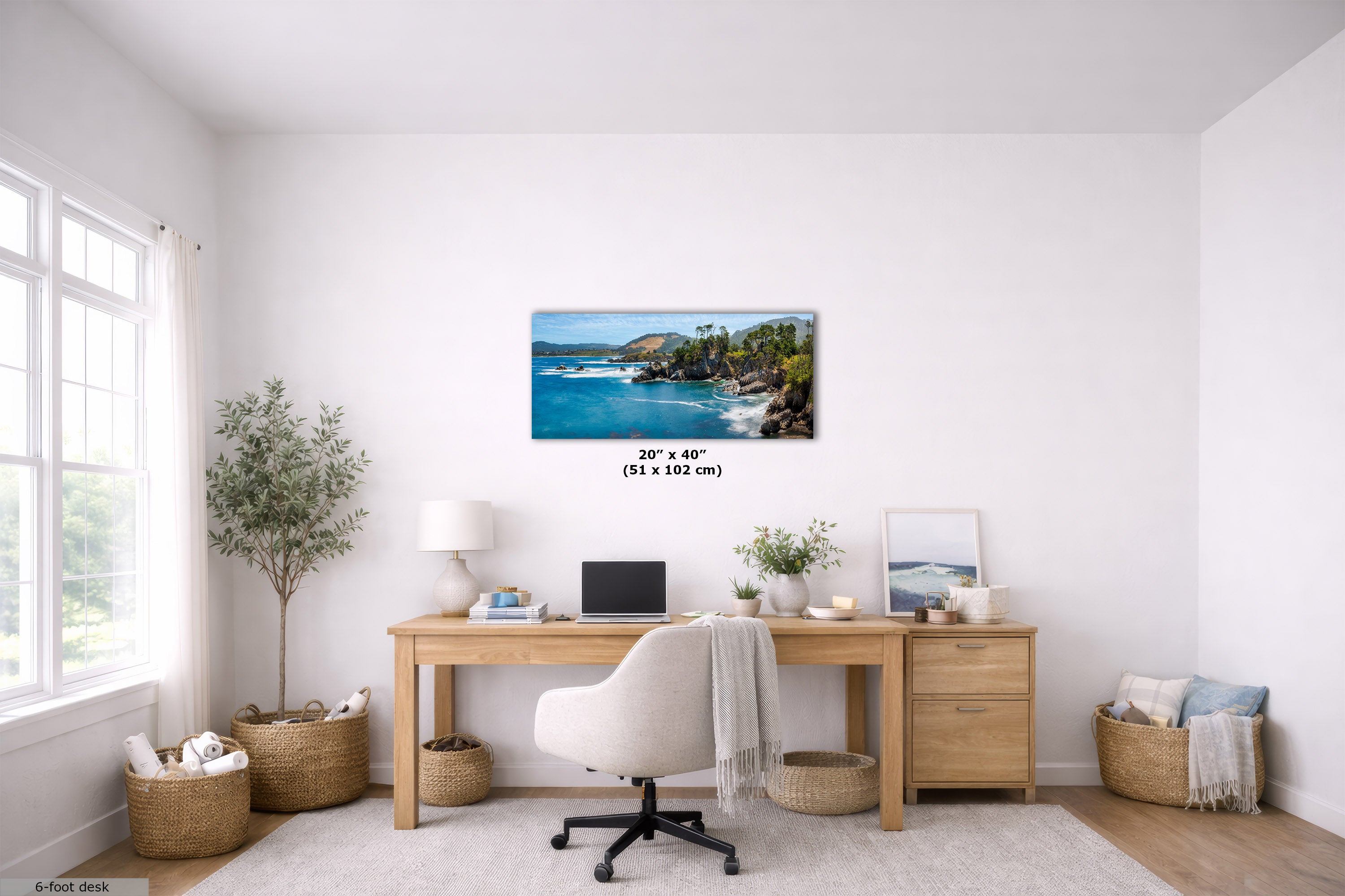 A framed coastal landscape wall art print hangs above a wooden desk in a bright, modern home office. The print depicts a tropical beach scene with blue water, green trees, and rocky cliffs.