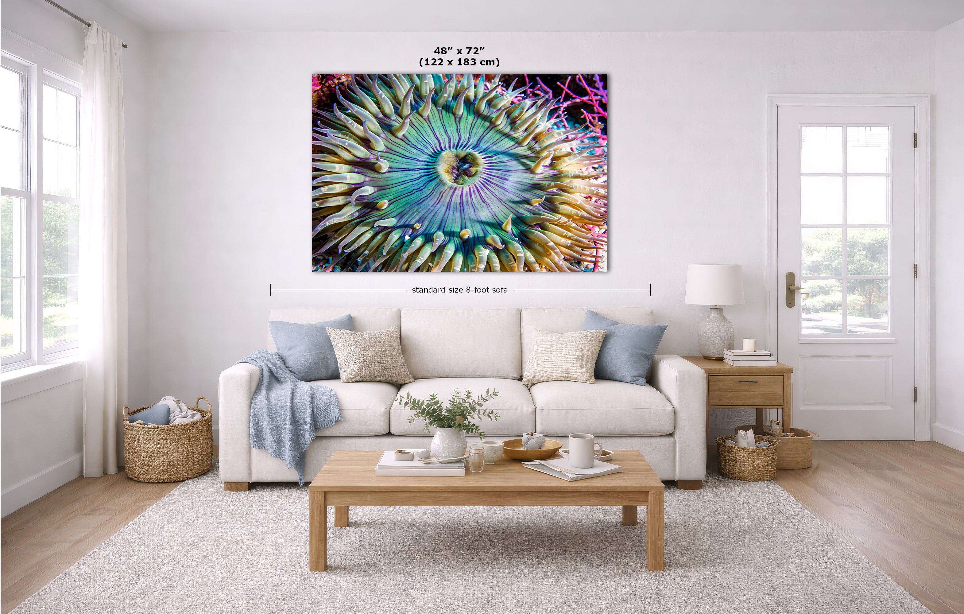 A colorful underwater anemone photograph wall art print displayed above a white sofa in a bright, modern living room. The artwork features a vibrant, multicolored spiral pattern with shades of blue, green, yellow, pink, and purple.