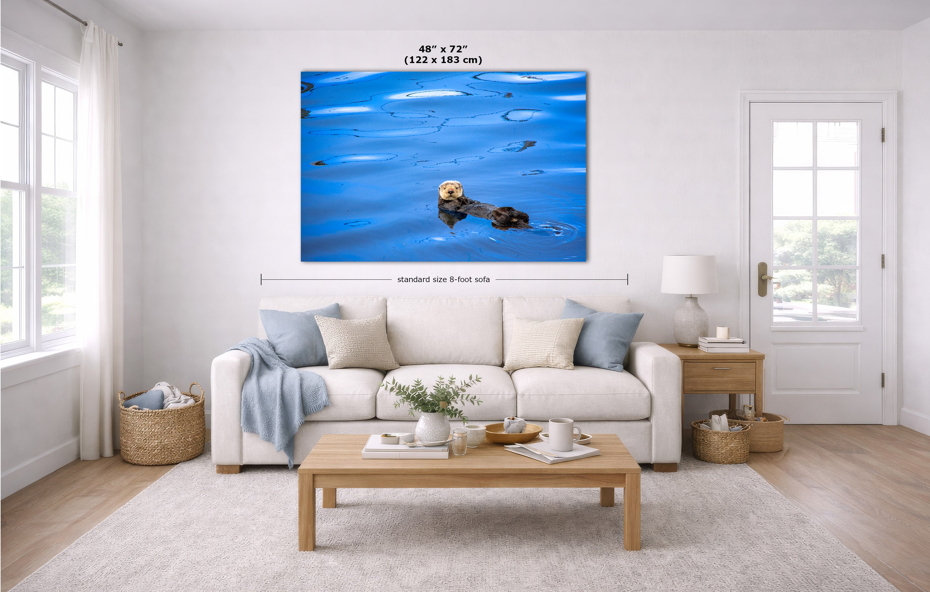 A large wall art print showing a bright blue scene with a sea otter is displayed above a white sofa in a modern living room. The print includes dimension labels indicating 48 x 72 inches.