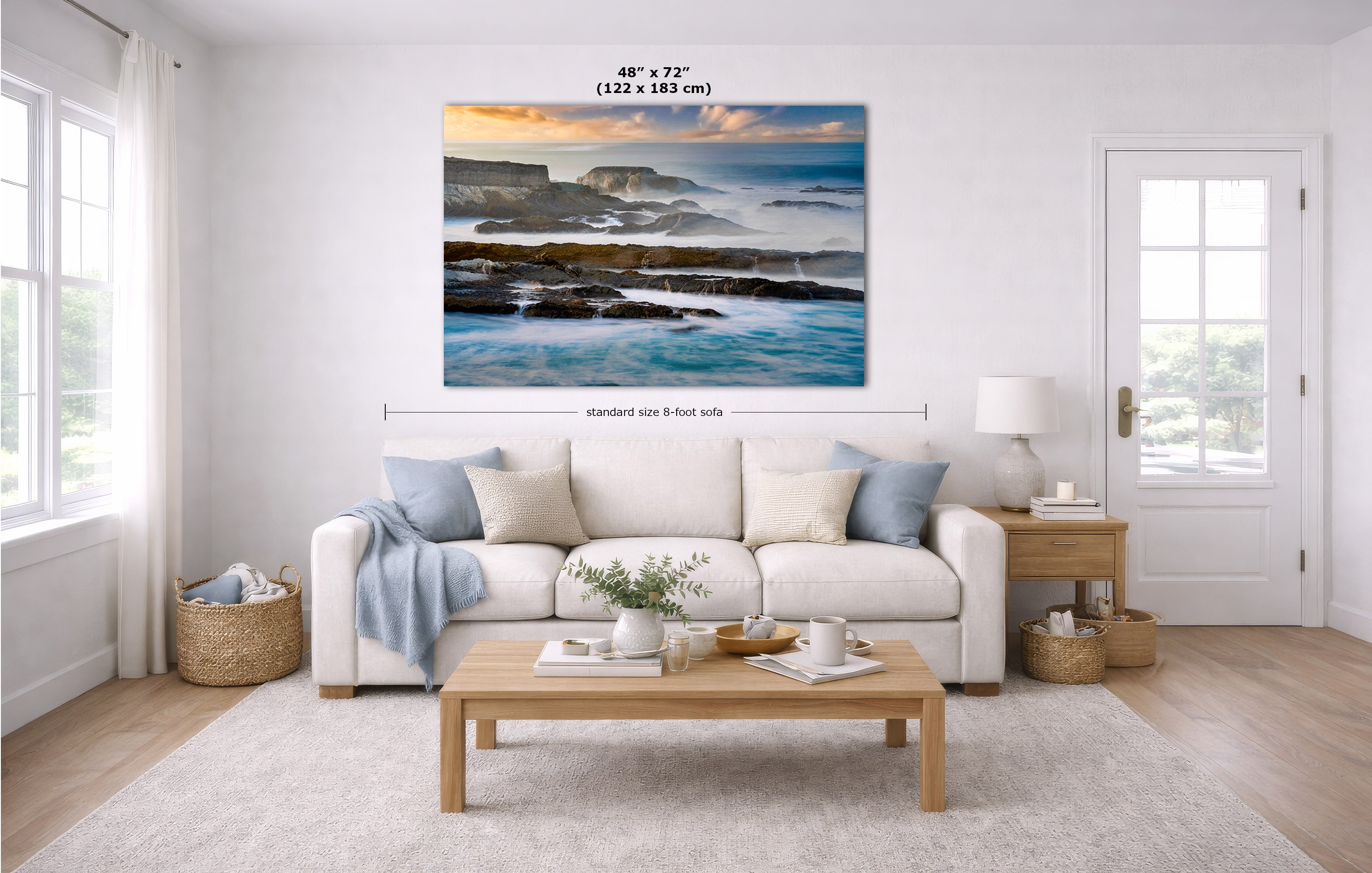 A large landscape canvas print of coastal cliffs and waves is displayed on a white wall in a bright, modern living room. The image includes dimension lines and text indicating the print's size as 48" x 72" (122 x 183 cm) and a standard 8-foot side width.