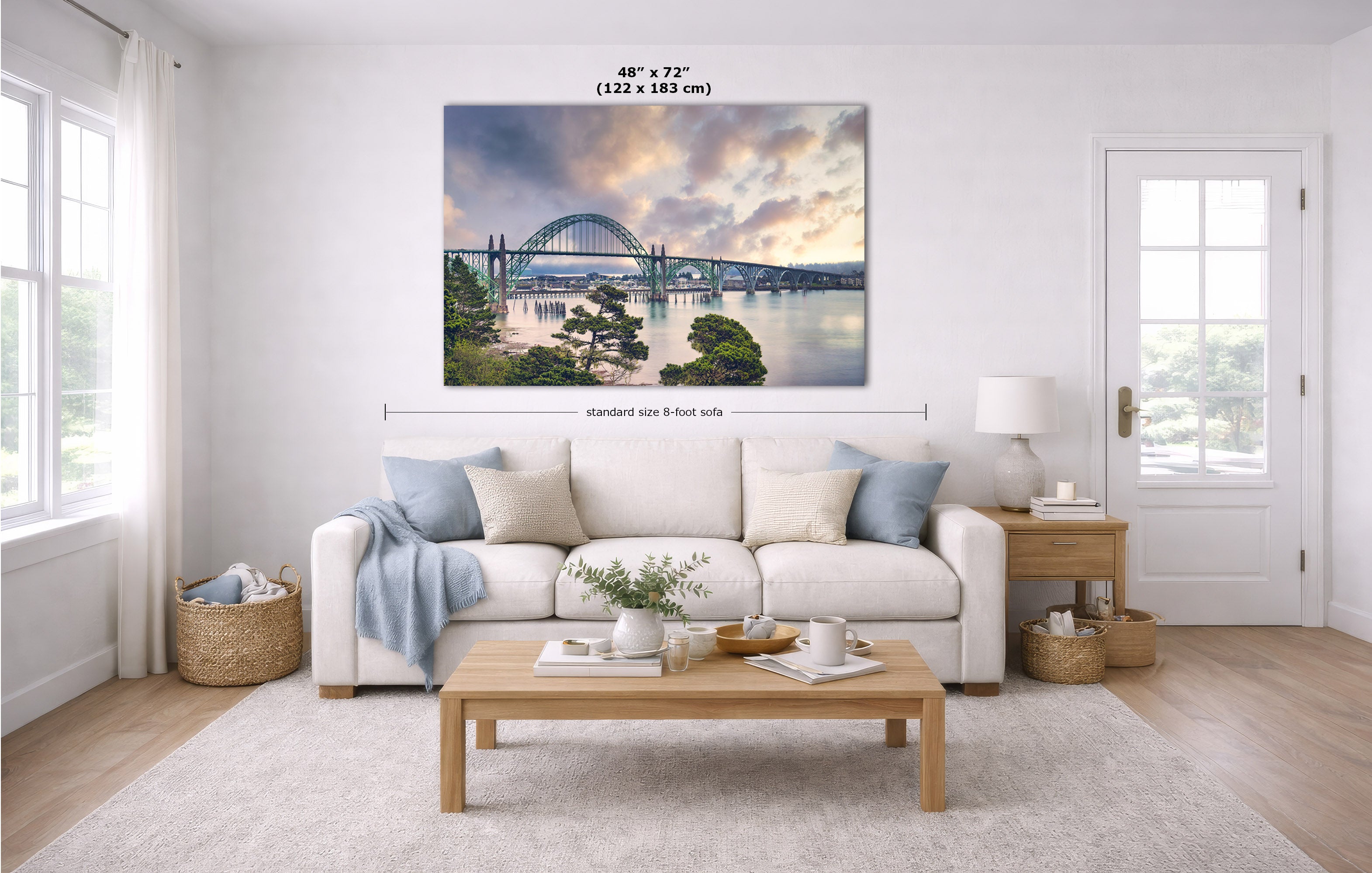 A large rectangular wall art print showing a bridge over water at sunset, displayed above a white sofa in a bright modern living room. Measurement lines and text indicate the print size as 48 x 72 inches.