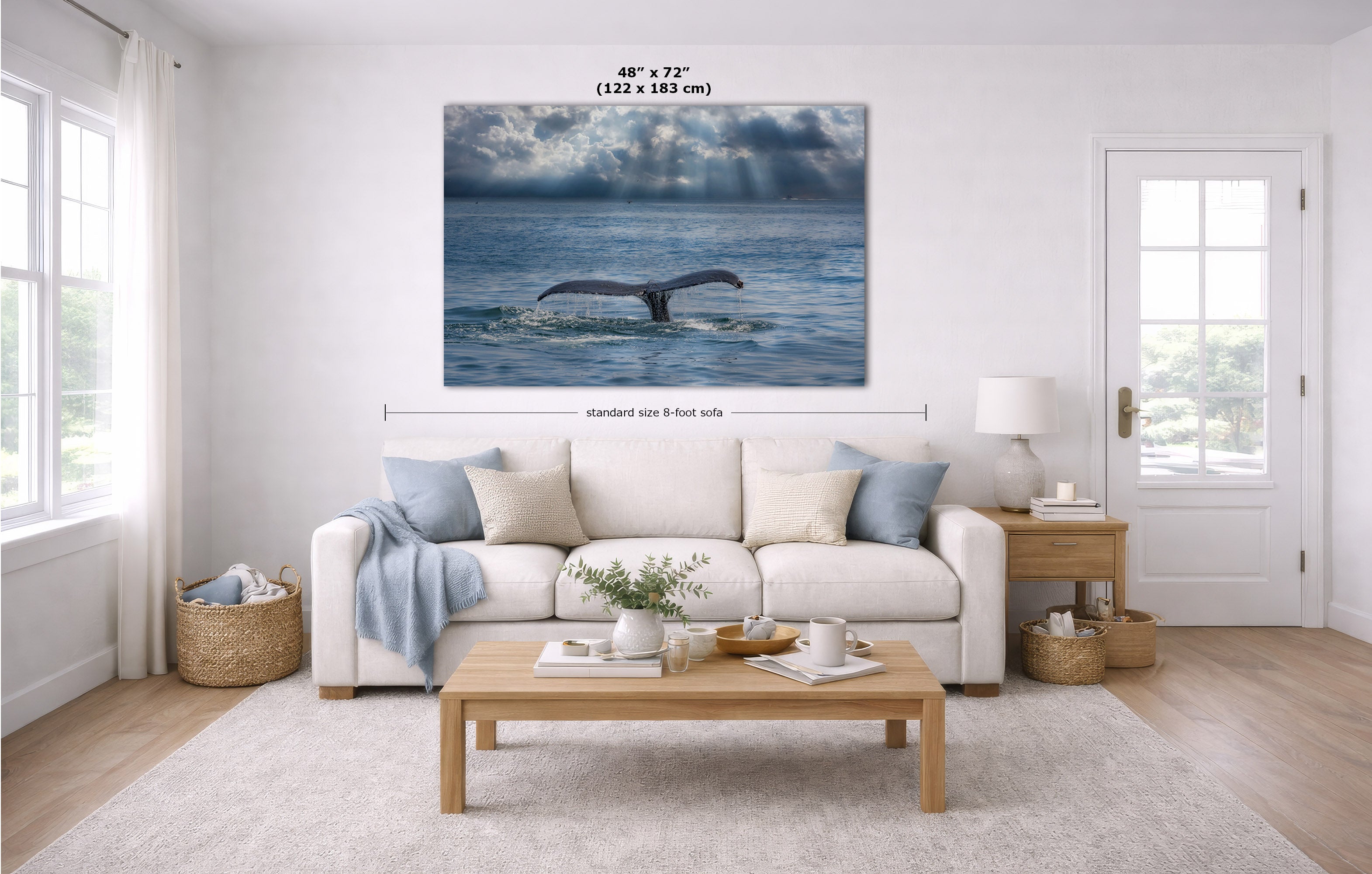 A large rectangular wall art print showing a whale tail diving in blue ocean water, displayed above a white sofa in a bright modern living room. Measurement lines and text indicate the print size as 48 x 72 inches (122 x 183 cm).