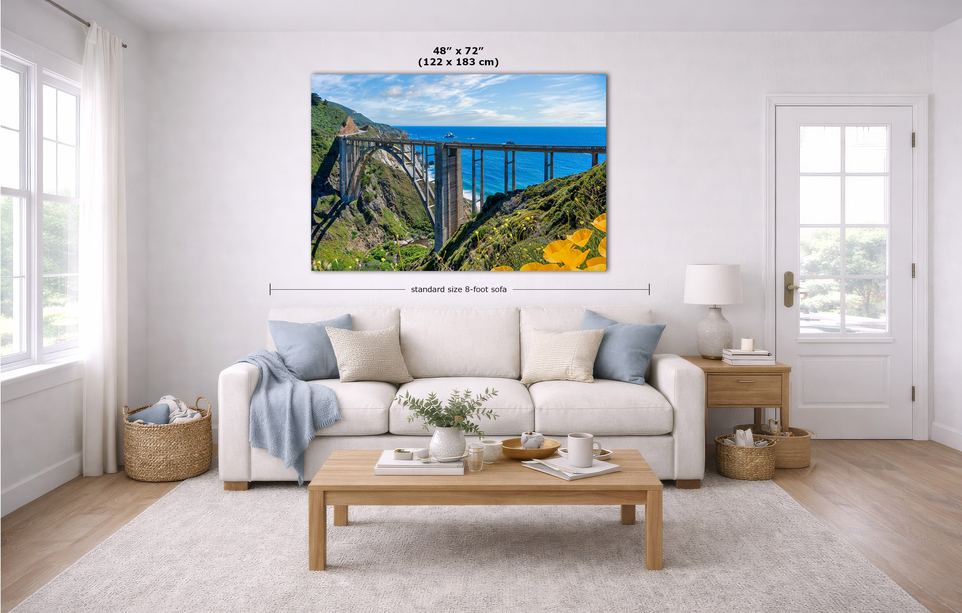 A wall art print showing a scenic bridge over blue water and green hills, displayed above a white sofa in a bright modern living room. Measurement labels indicate the print size as 48 x 72 inches.