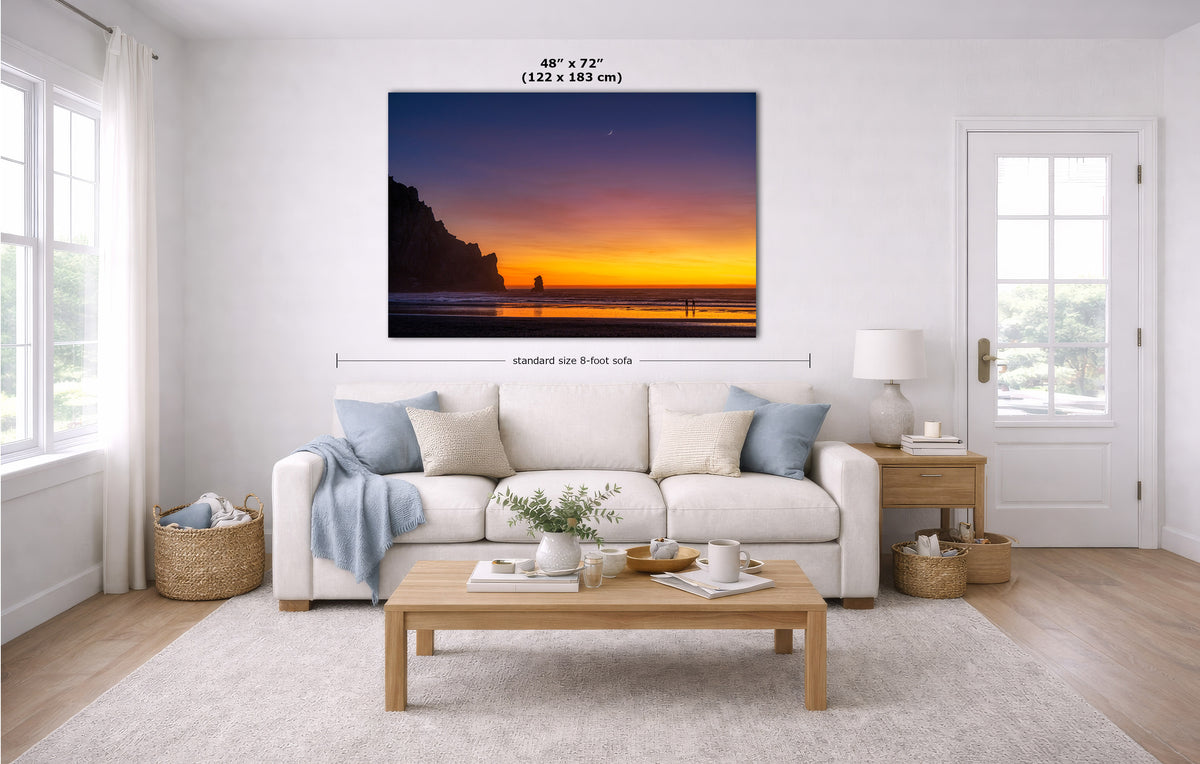 A large wall art print showing a sunset over cliffs and water, displayed above a white sofa in a bright modern living room. Black measurement text and arrows indicate the print size as 48 x 72 inches (122 x 183 cm) and note a standard 8-foot side width.