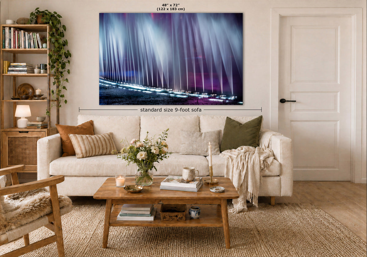 A large rectangular wall art print showing vertical light beams in blue, purple, and pink tones, displayed above a cream sofa in a styled living room. White dimension lines indicate the print is 48 x 72 inches, with text reading 'standard size 9-foot sofa'.
