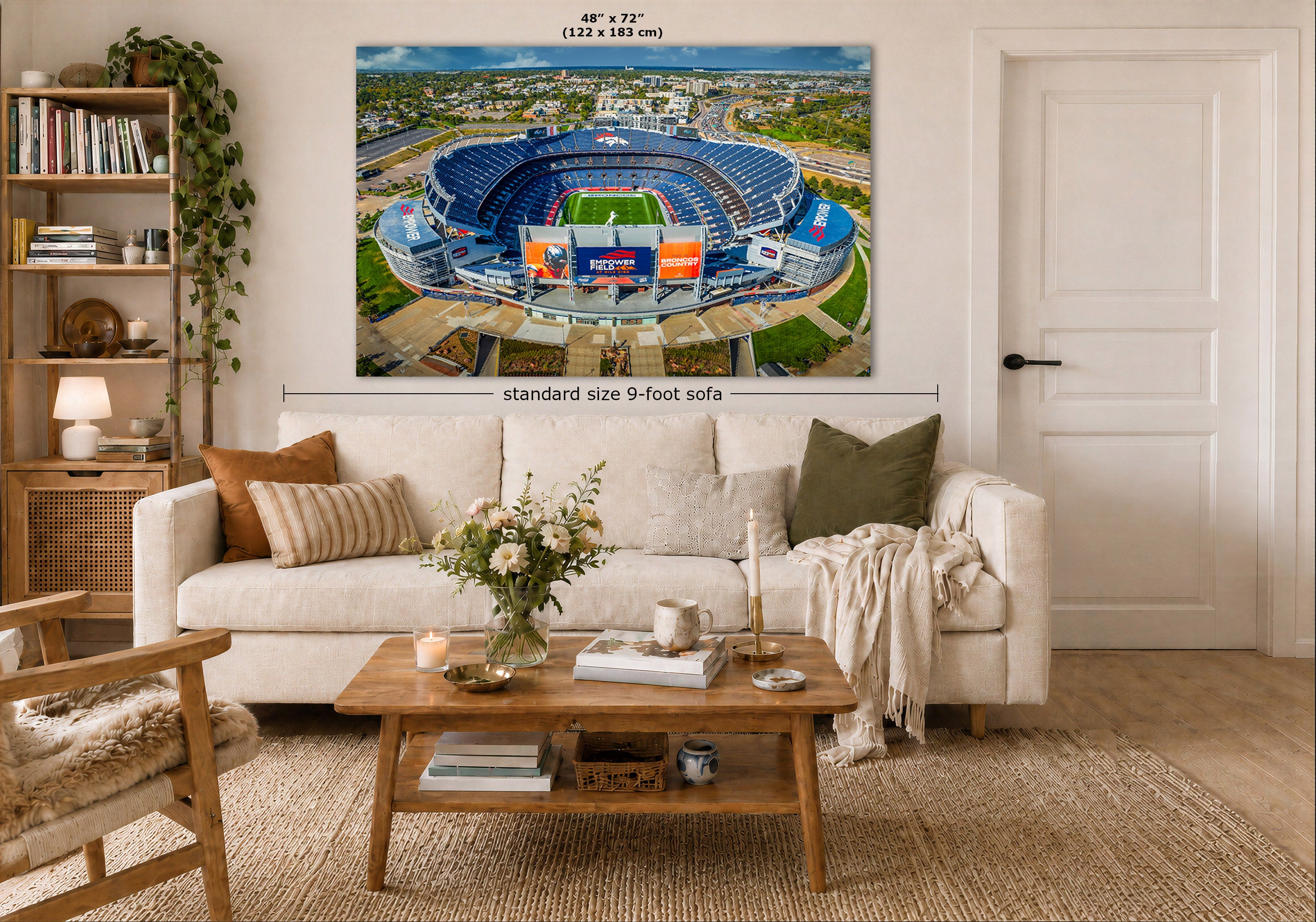 A Denver Broncos Stadium art print showing an aerial view of the Denver Broncos Mile High stadium, displayed above a white sofa in a styled living room. The print includes size markings reading 48 x 72 inches and 'standard size 9-foot sofa'.