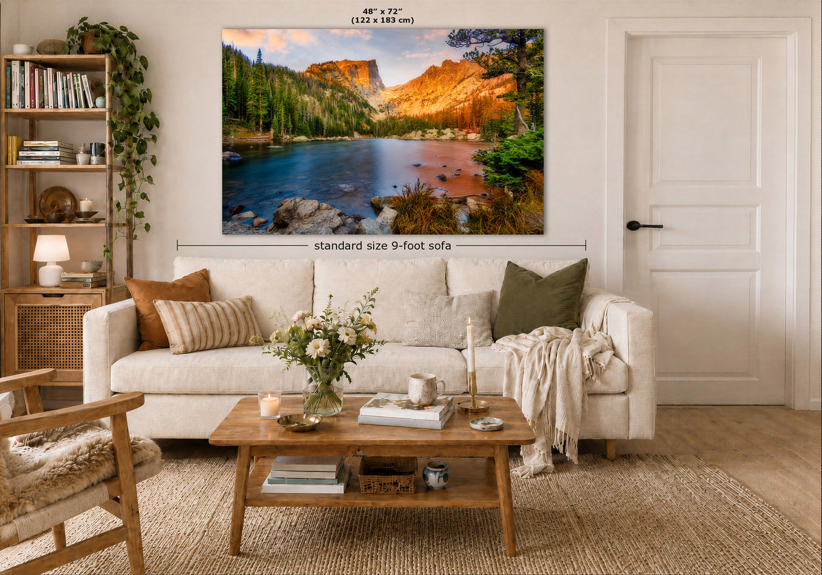 A large wall art print showing a colorful mountain lake landscape is displayed above a white sofa in a styled living room. The print includes dimension labels reading 48 x 72 inches and a note about standard size 9-foot sofa.