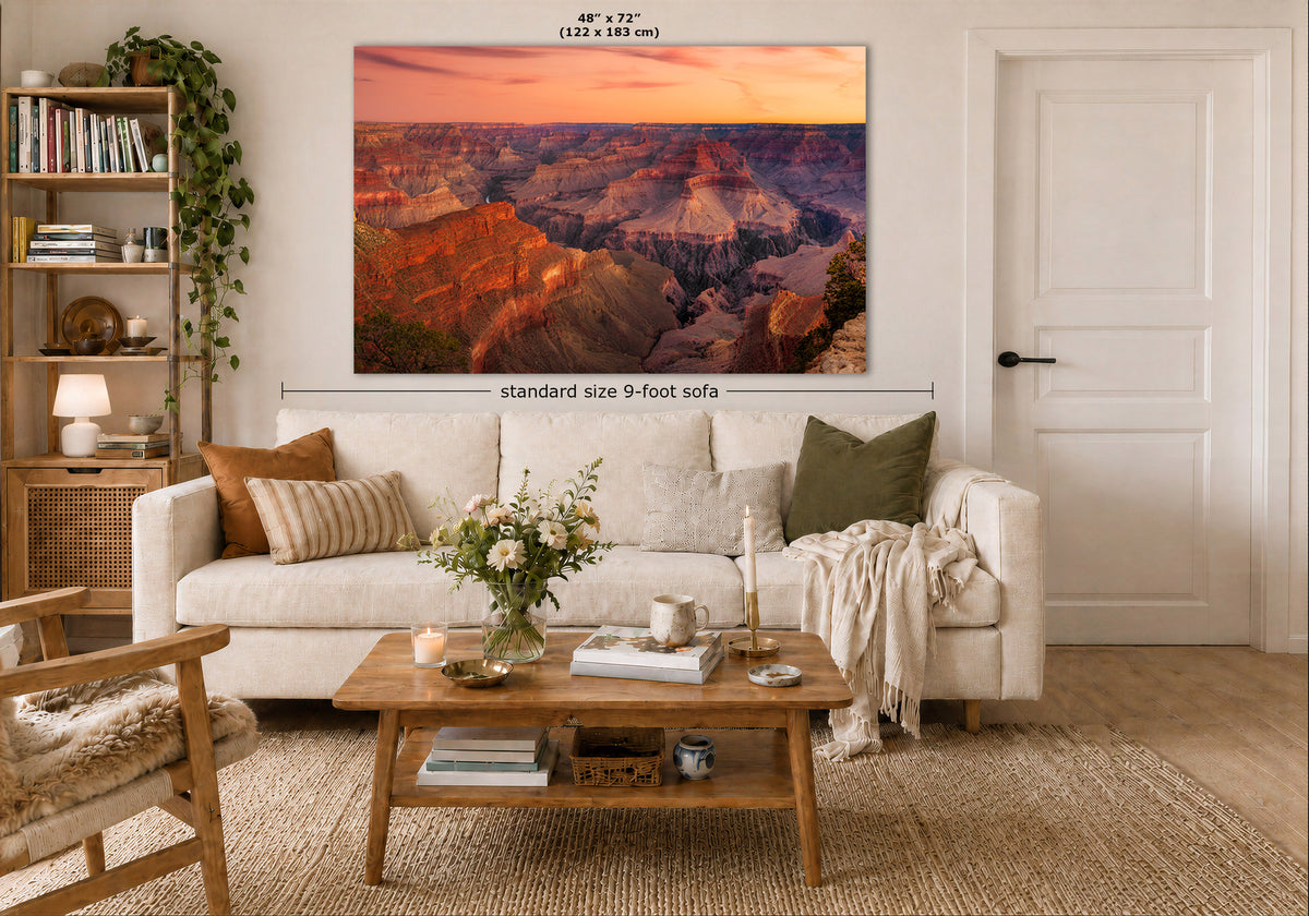 A large rectangular wall art print showing a canyon landscape at sunset hangs above a white sofa in a styled living room. The image includes dimension labels indicating the print is 48 x 72 inches and the sofa is standard size 9-foot wide.