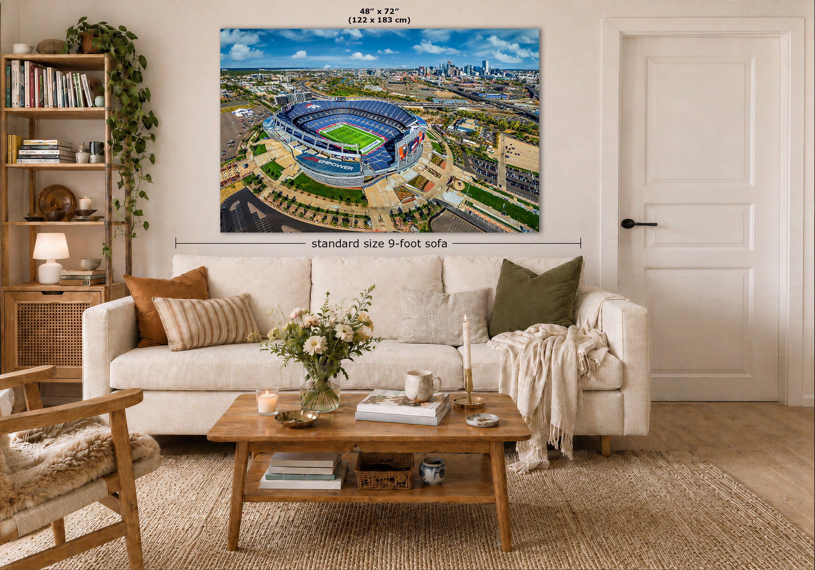 A large Empower Field Denver skyline panorama wall art print showing an aerial view of the Denver Broncos Stadium and city skyline, displayed above a white sofa in a styled living room. The print includes size markings reading 48 x 72 inches and a dimension note for a standard size 9-foot sofa.