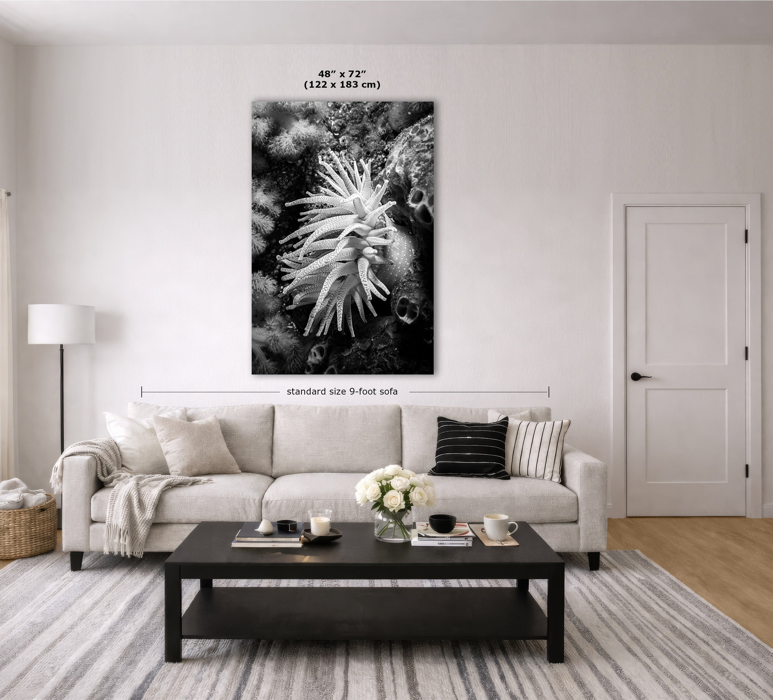 A black and white wall art print of a sea anemone displayed in a modern living room mockup above a light beige sofa, with dimension lines and text indicating the size is 48 x 72 inches (122 x 183 m).