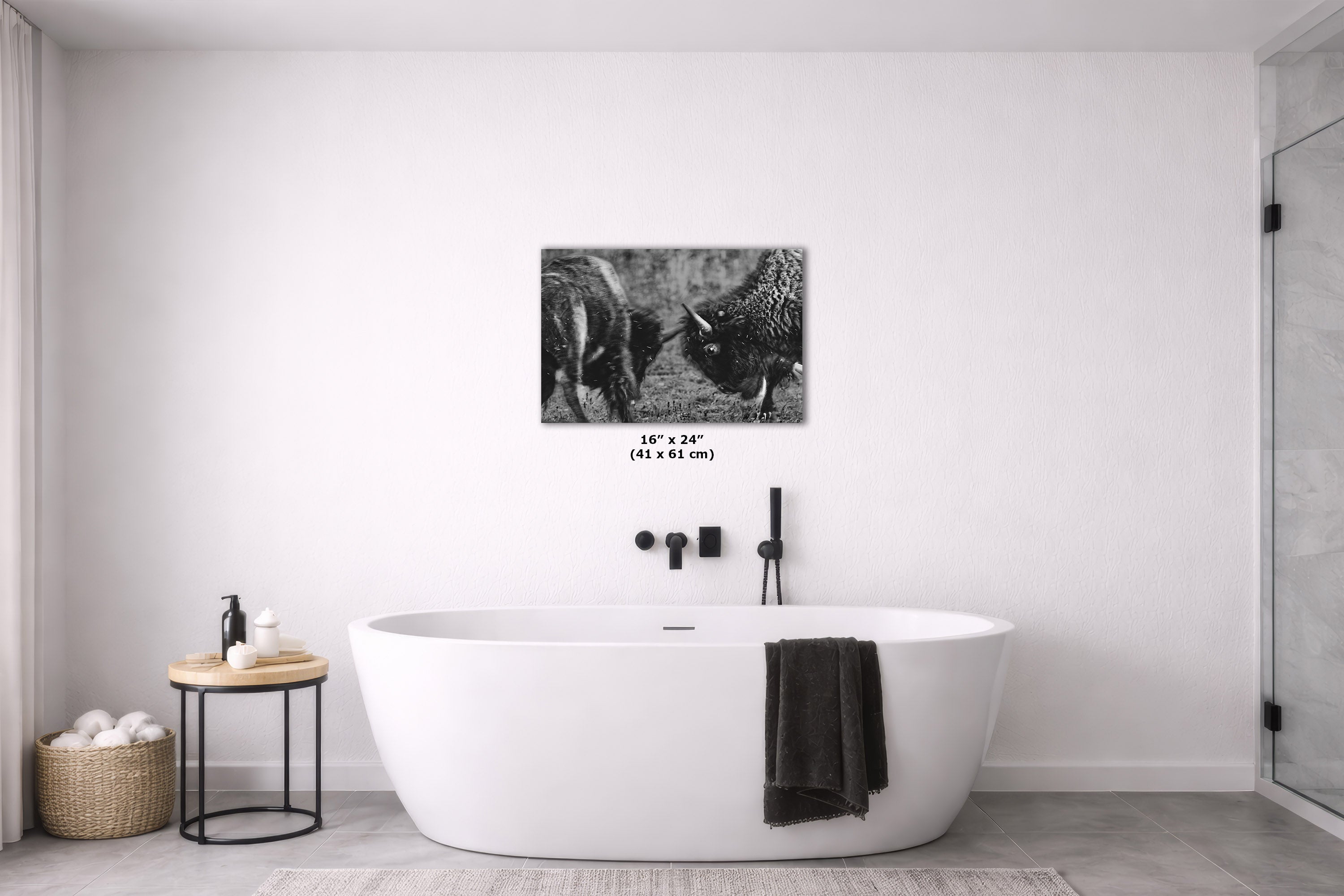 A black and white animal print canvas wall art print depicting two buffalo, displayed in a modern bathroom setting above a white freestanding bathtub.
