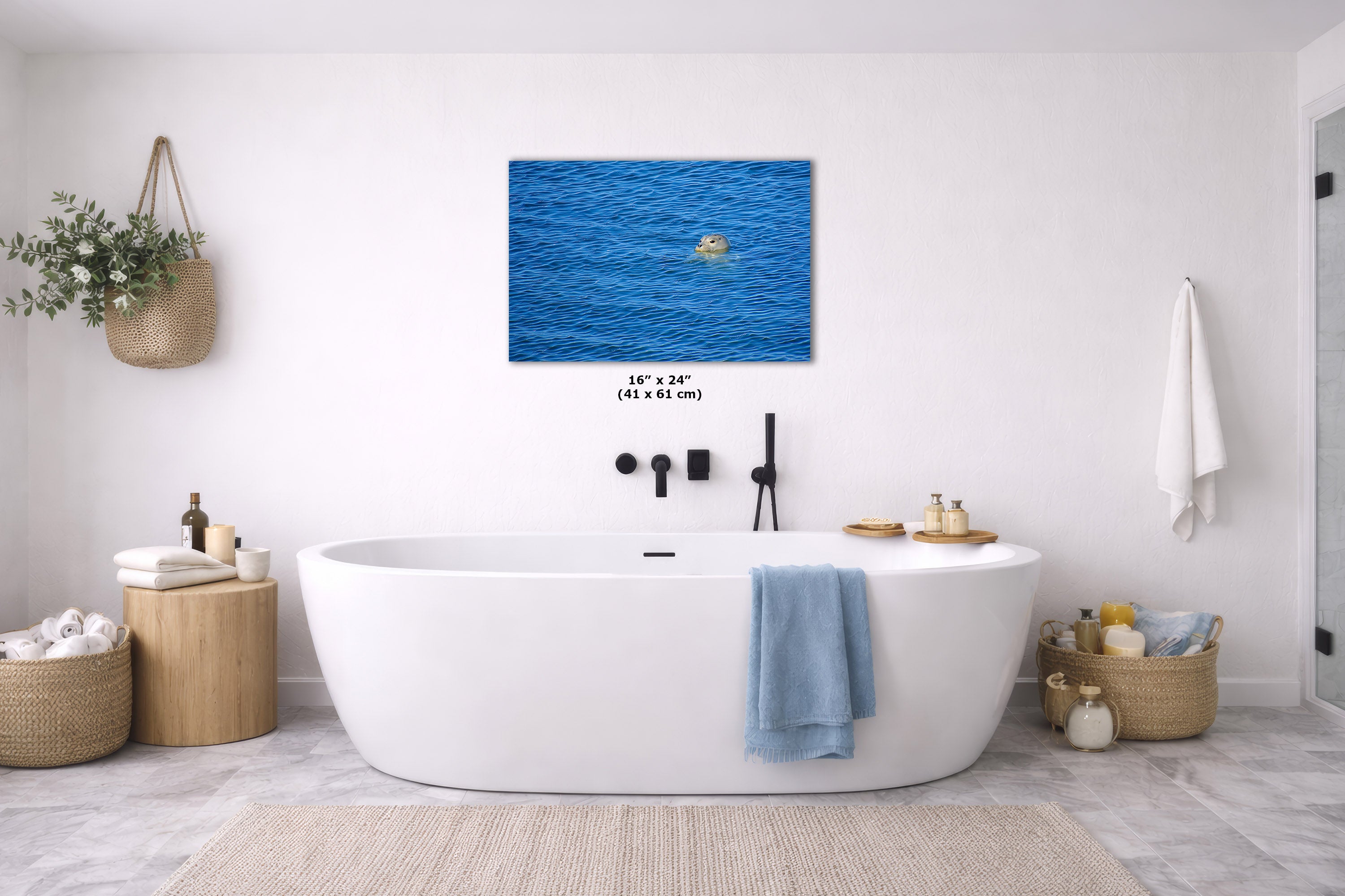 A wall art print depicting a bright blue ocean with a small yellow boat, displayed above a white freestanding bathtub in a bright, modern bathroom. The print includes size text reading 16" x 24" (41 x 61 cm).