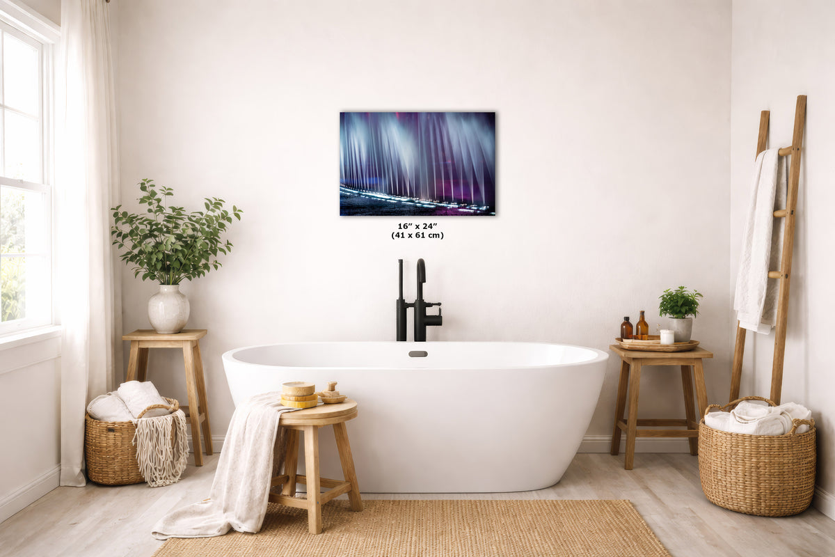 A freestanding white bathtub in a bright, neutral-toned bathroom with a wall-mounted colorful art print above it. The room includes wooden stools, woven baskets, plants, and a ladder-style towel rack.