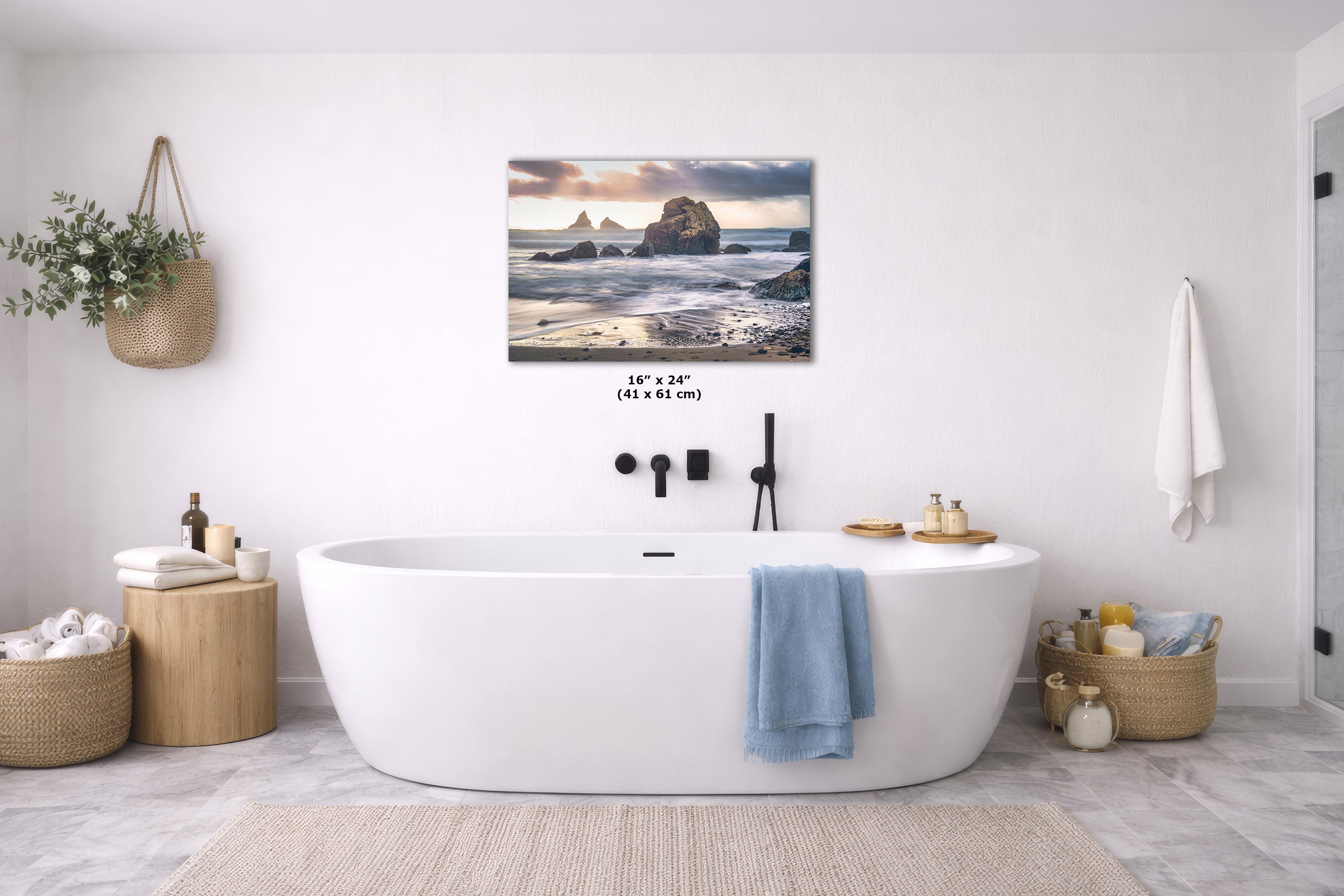 A wall art print showing a rocky beach and ocean scene hangs above a white freestanding bathtub in a bright, modern bathroom. The print is the product being sold, but the room setting is clearly visible, so this is Lifestyle rather than Product/Packaging.