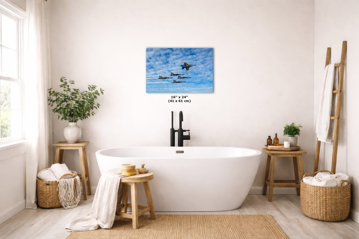 A wall art print showing fighter jets flying through a blue sky with clouds, displayed above a white freestanding bathtub in a bright, modern bathroom with wooden stools, plants, and woven baskets.