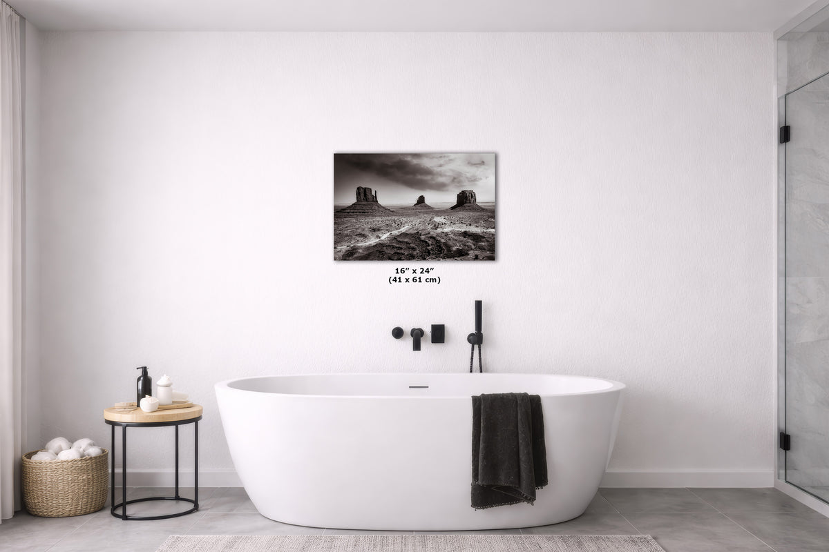 A black and white landscape art print of Monument Valley is displayed on a white wall above a modern freestanding bathtub in a minimalist bathroom setting.