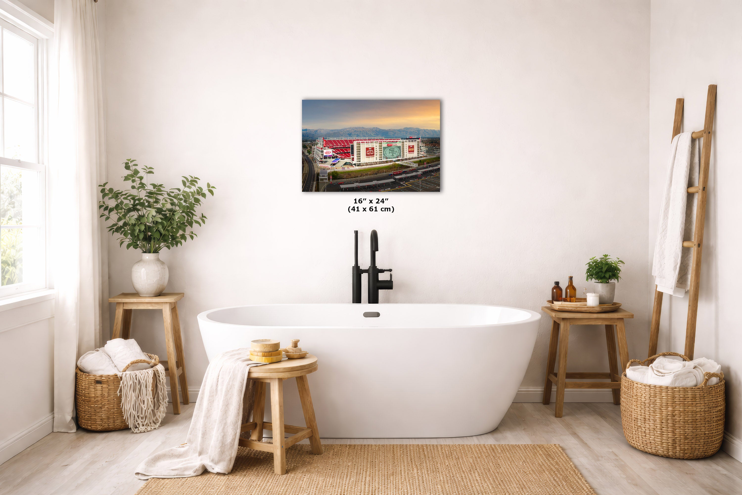 A freestanding bathtub in a bright, modern bathroom with a wall-mounted city skyline art print above it. The room includes wooden stools, woven baskets, plants, and a ladder shelf with towels.