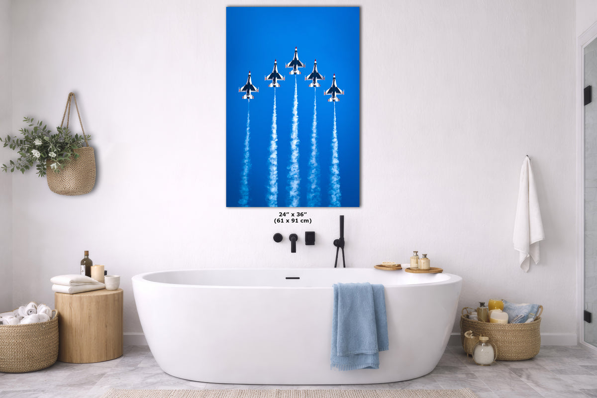 A vertical canvas wall art print depicting six fighter jets flying in a blue sky with white contrails, displayed in a modern white bathroom above a freestanding bathtub.