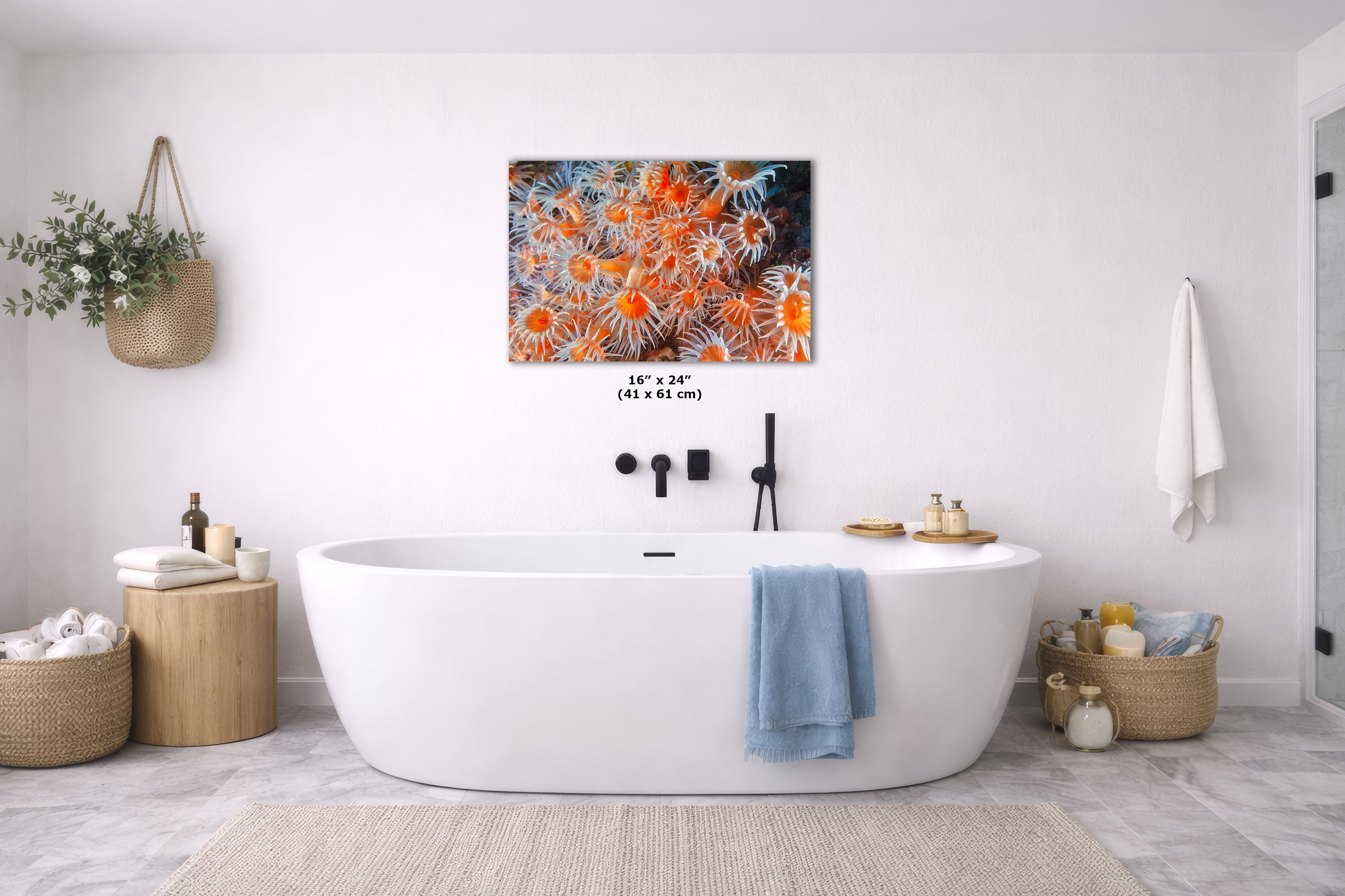 A freestanding oval bathtub in a bright white bathroom, with a colorful abstract wall art print above it. The artwork features orange, black, and cream floral or coral-like patterns.