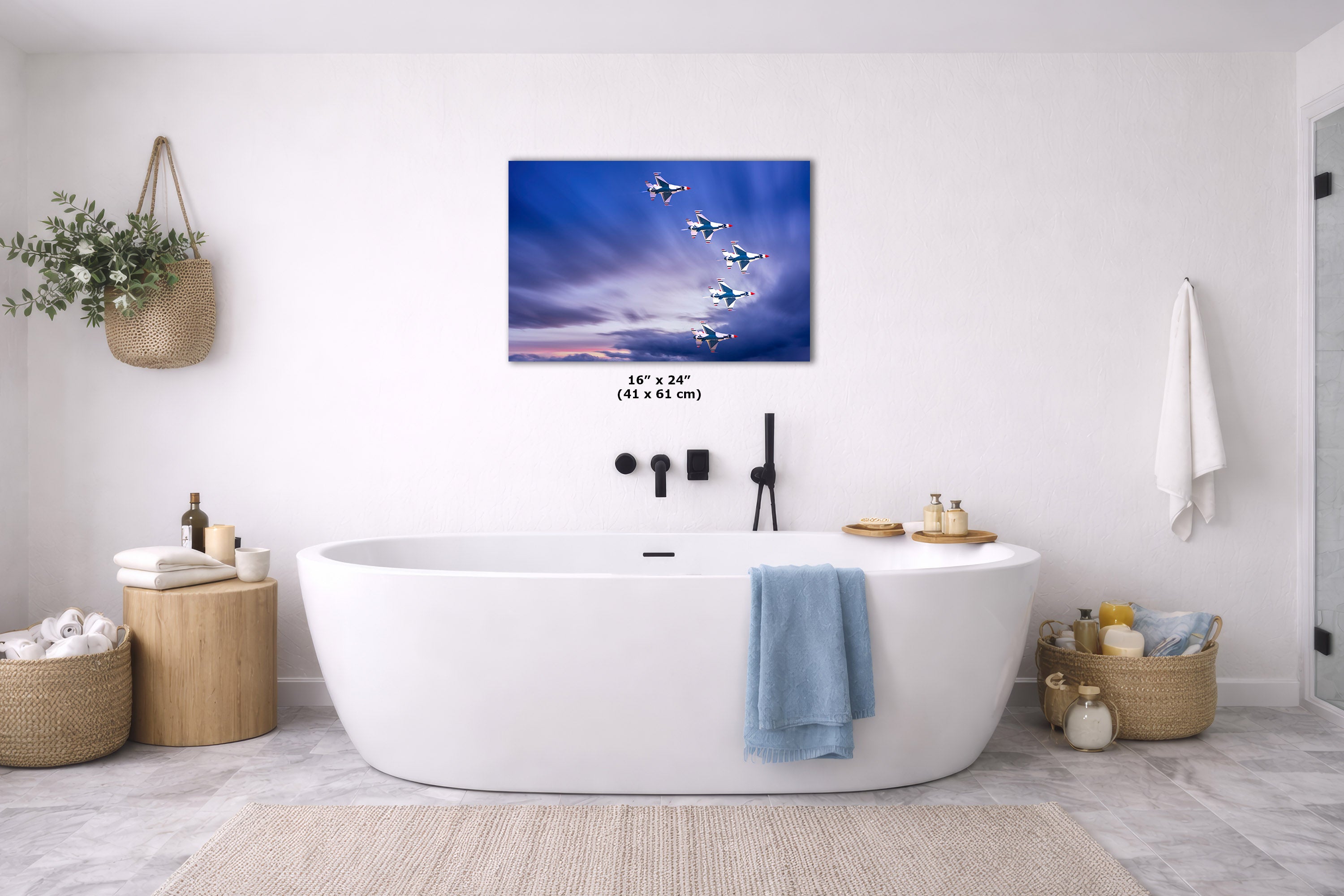 A wall art print showing a blue sky with several airplanes flying, displayed above a white freestanding bathtub in a bright modern bathroom. The print includes size text reading 16 x 24 in.
