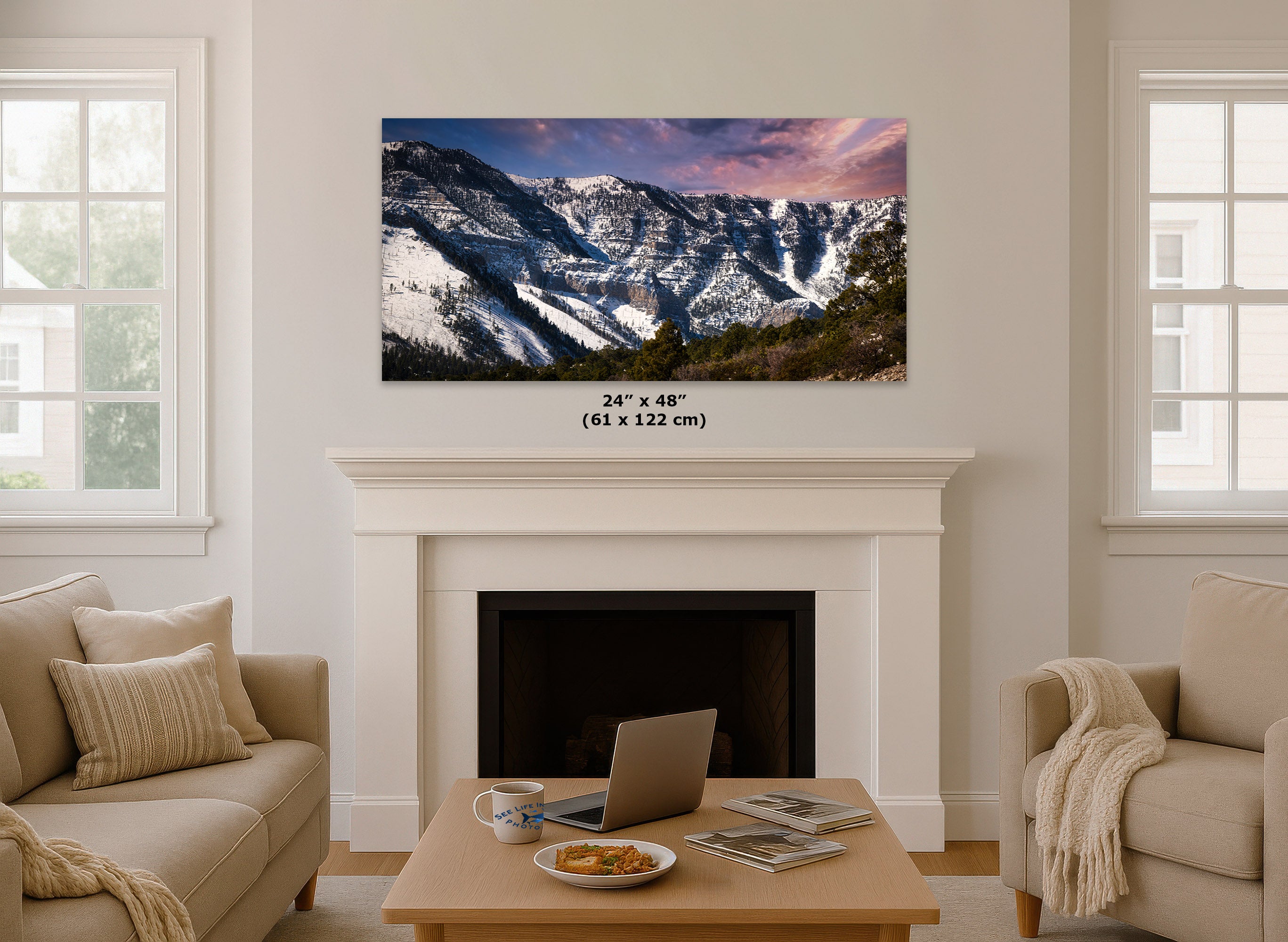 A 24x48 inch landscape wall art print of snowy mountains under a pink and purple sunset sky, displayed on a white fireplace mantel in a bright, modern living room. The dimensions are printed in black text below the print.