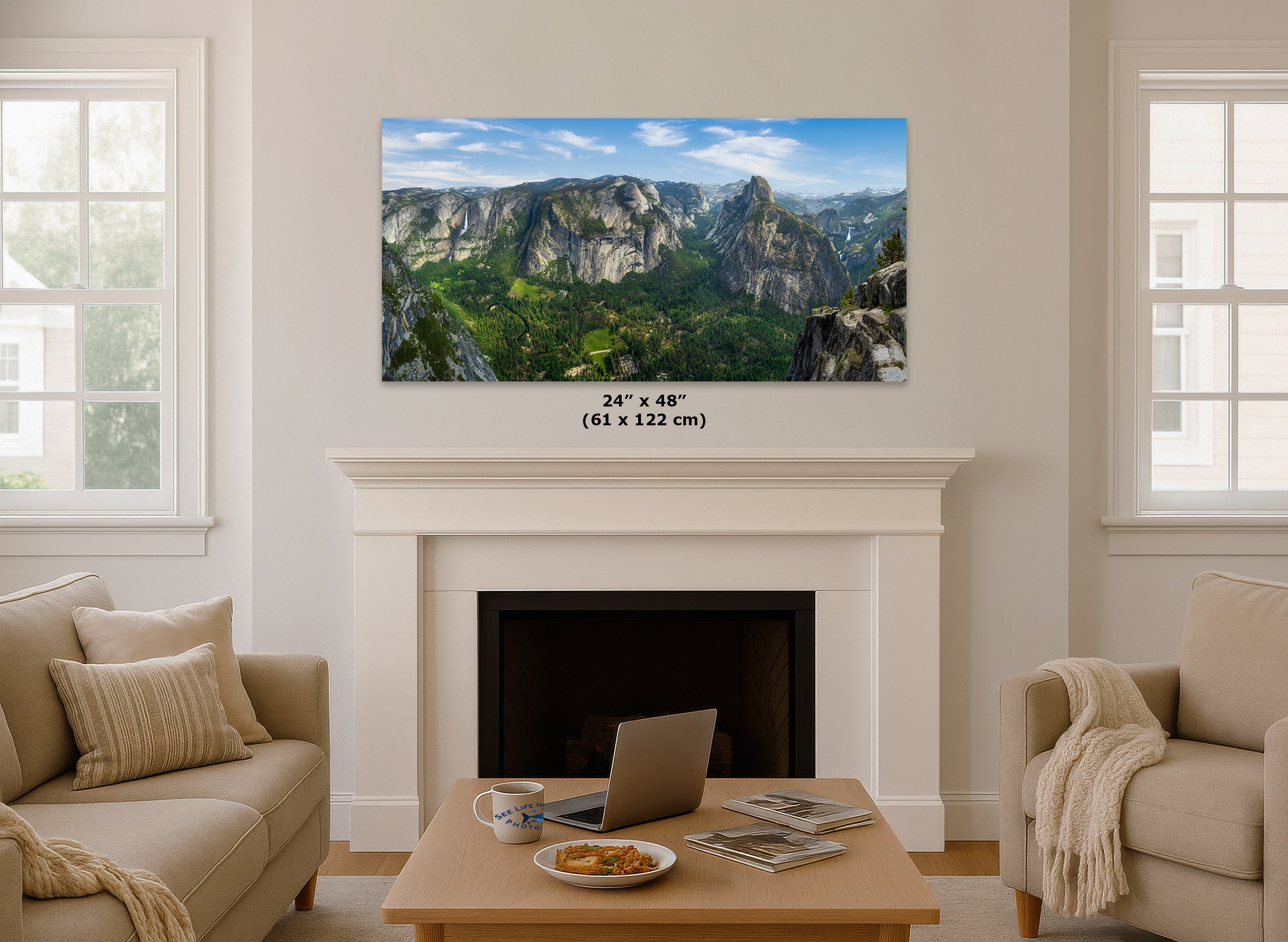 A wall art print showing a mountain valley landscape hangs above a white fireplace in a bright living room. The print includes size text reading 24 x 48 inches (61 x 122 cm).