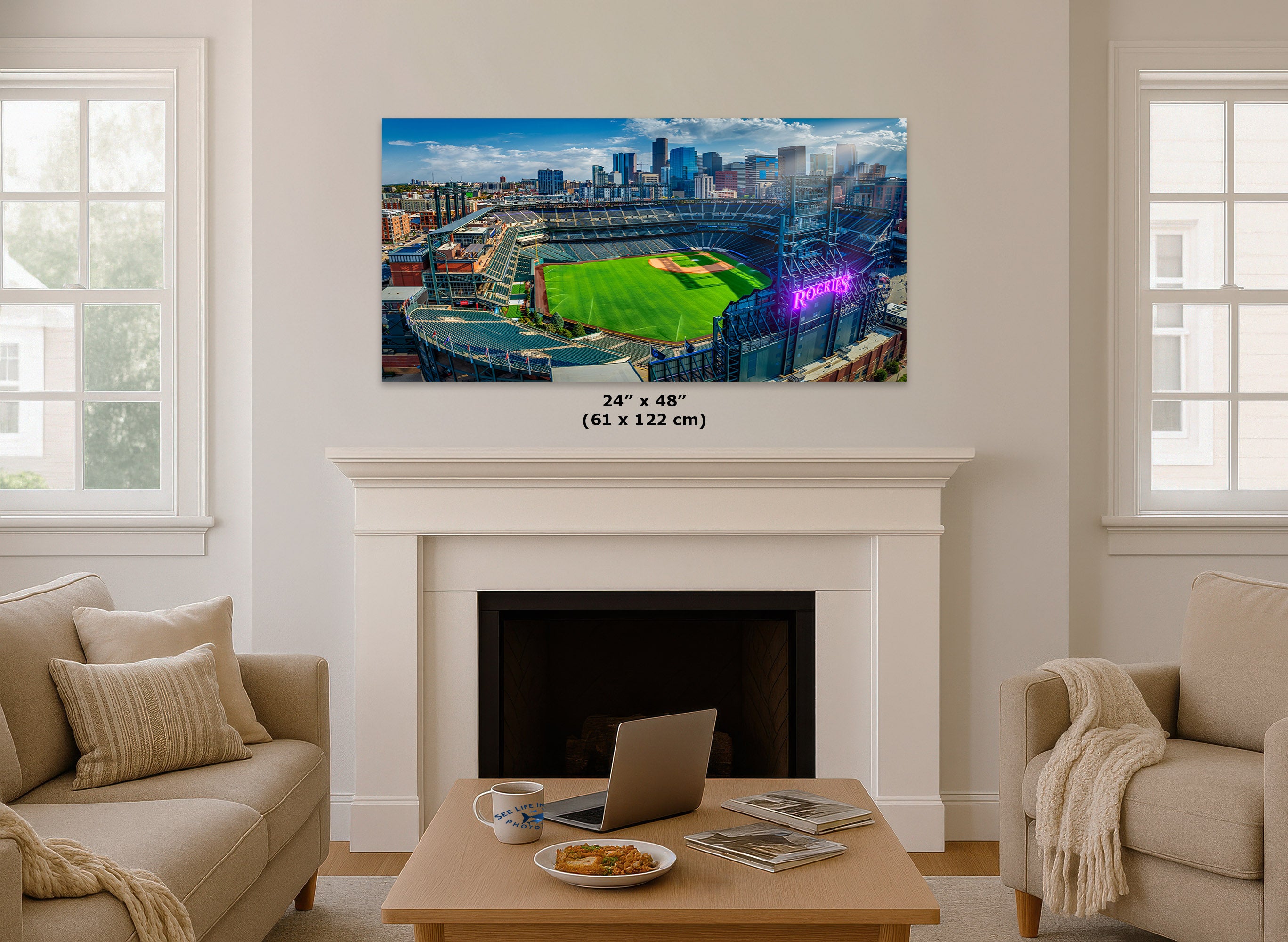 A wall art print showing a baseball stadium cityscape hangs above a white fireplace in a bright living room. The print includes size text reading 24 x 48 inches (61 x 122 cm).