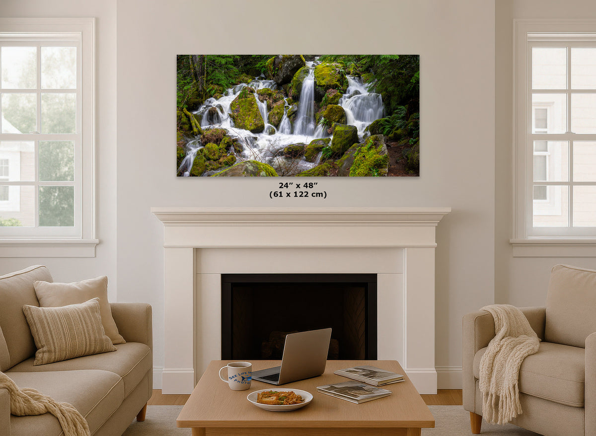 An Oregon waterfall panorama print showing a lush green waterfall landscape, displayed above a white fireplace mantel in a bright, modern living room. The print includes a size measurement overlay reading '24" x 48" (61 x 122 cm)'.