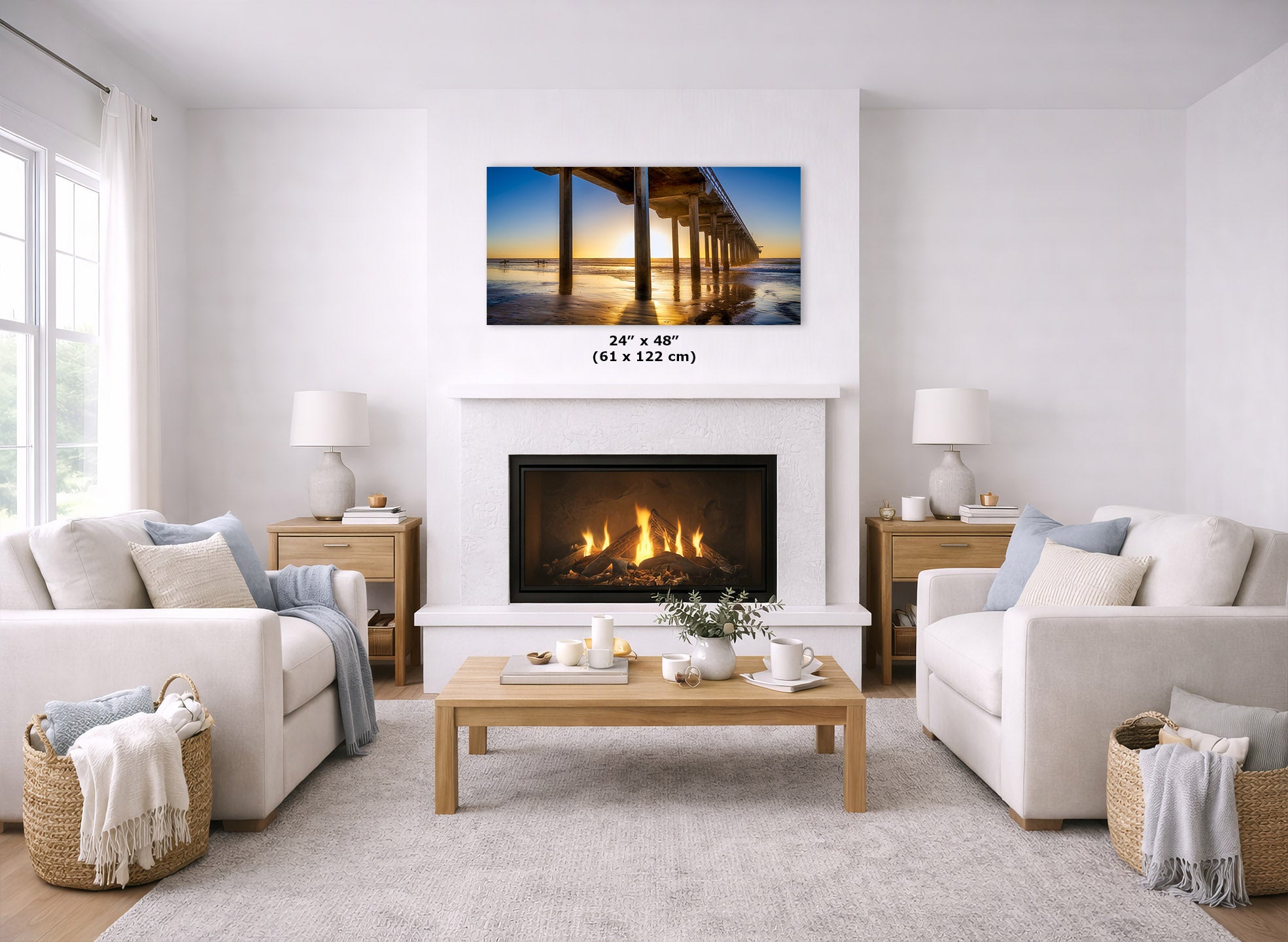 A framed wall art print showing a pier over water at sunset, displayed above a fireplace in a bright, modern living room. The print includes a size overlay reading 24" x 48" (61 x 122 cm).