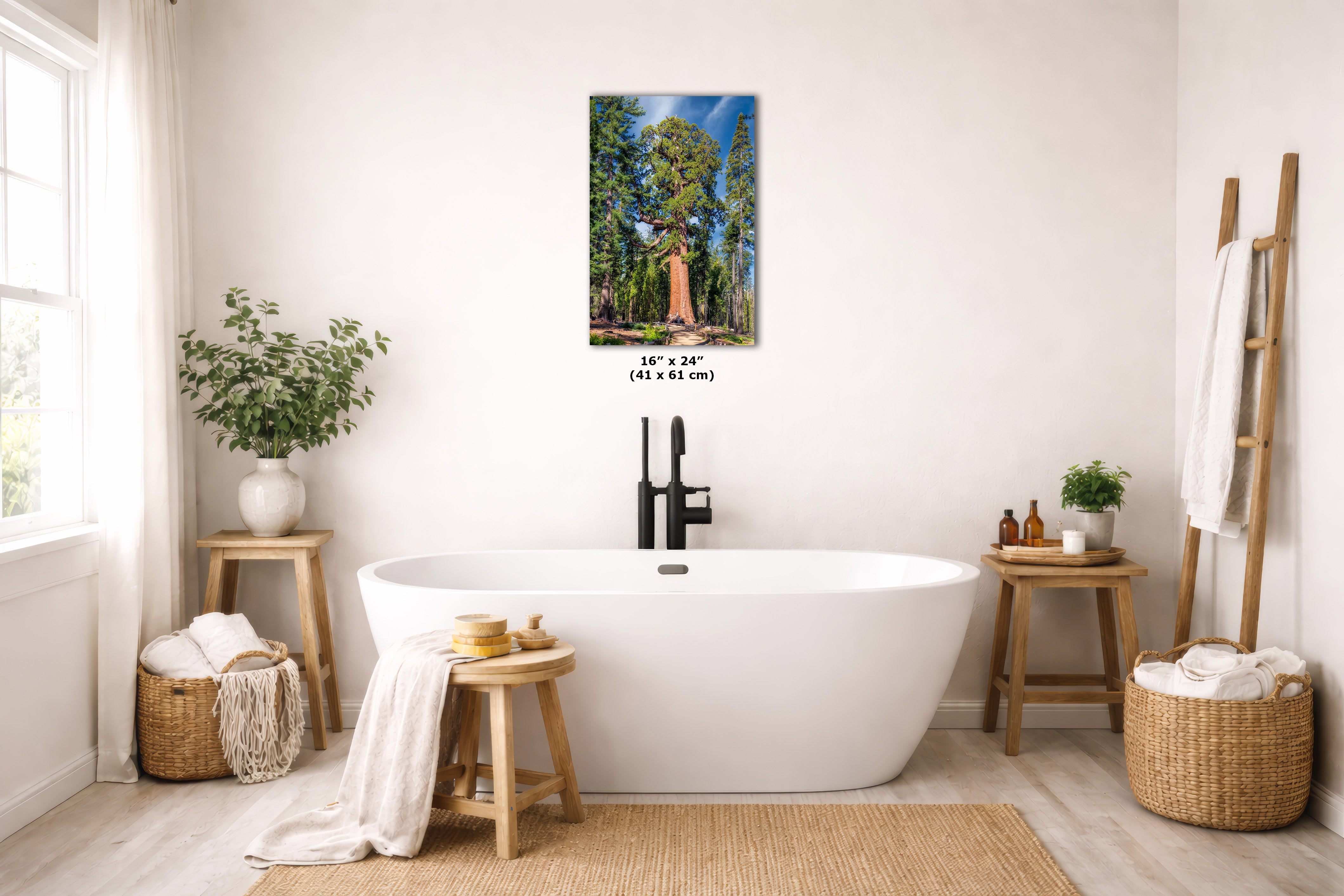 A framed vertical landscape art print depicting a canyon river scene, displayed on a light beige wall above a white freestanding bathtub in a bright, modern bathroom setting.