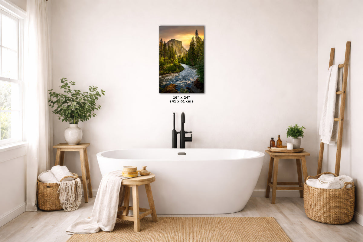 A vertical landscape art print depicting a scenic river flowing through a pine forest at sunset, displayed on a bathroom wall above a white freestanding bathtub. The print includes a size dimension overlay in the center.