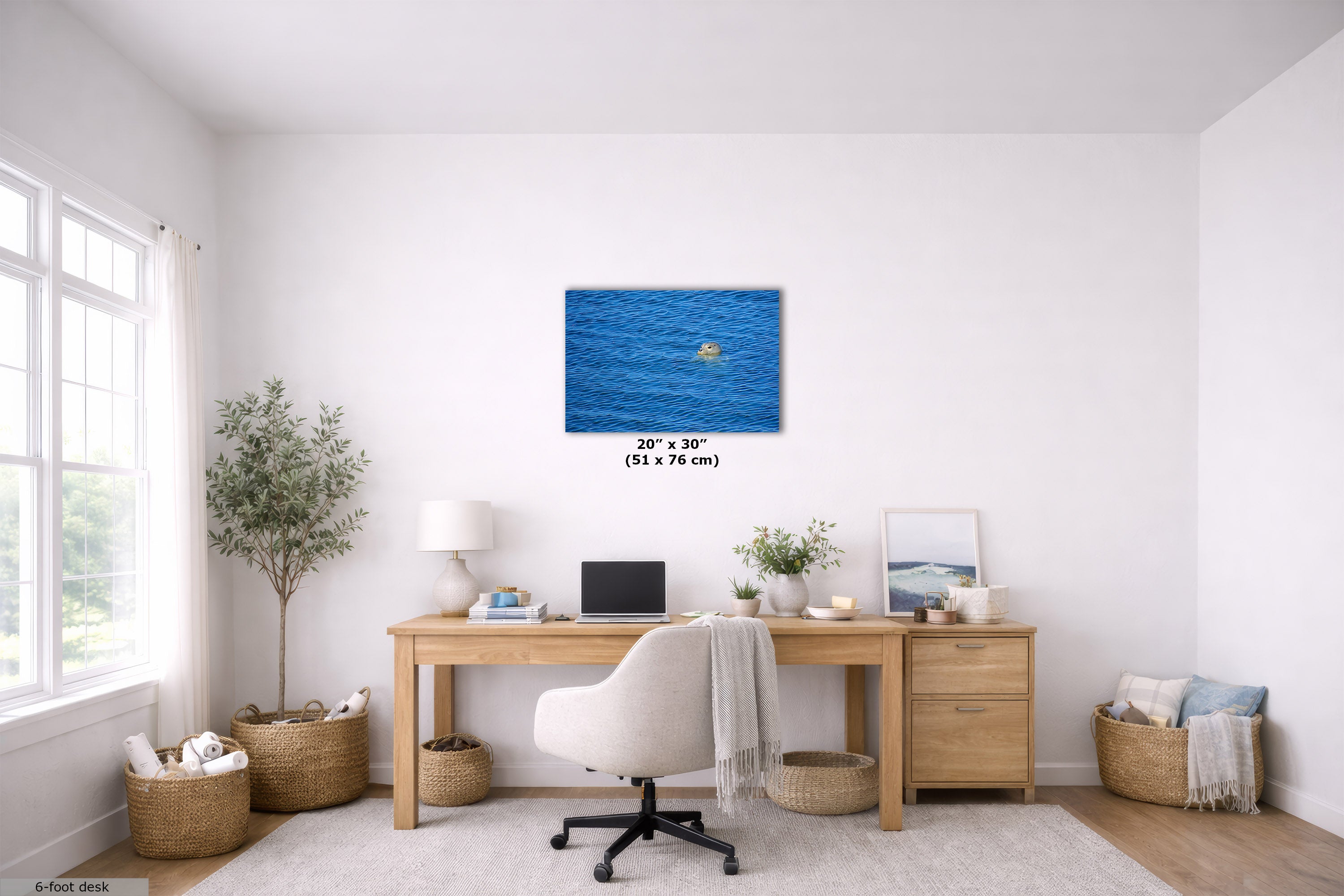 An art print depicting the head of a seal swimming in the ocean, displayed on a white wall in a modern, bright home office setting above a wooden desk.