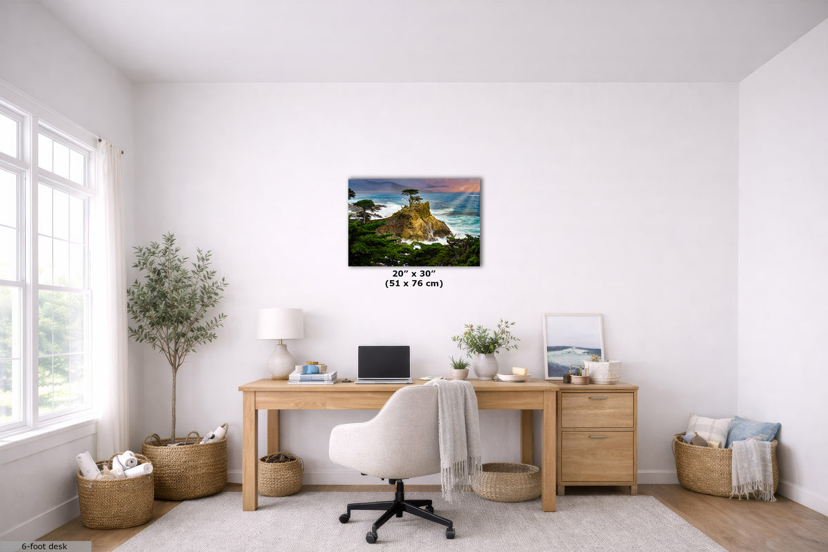 A coastal landscape wall art print hangs above a wooden desk in a bright, modern home office. The print depicts a rocky cliff overlooking the ocean at sunset.