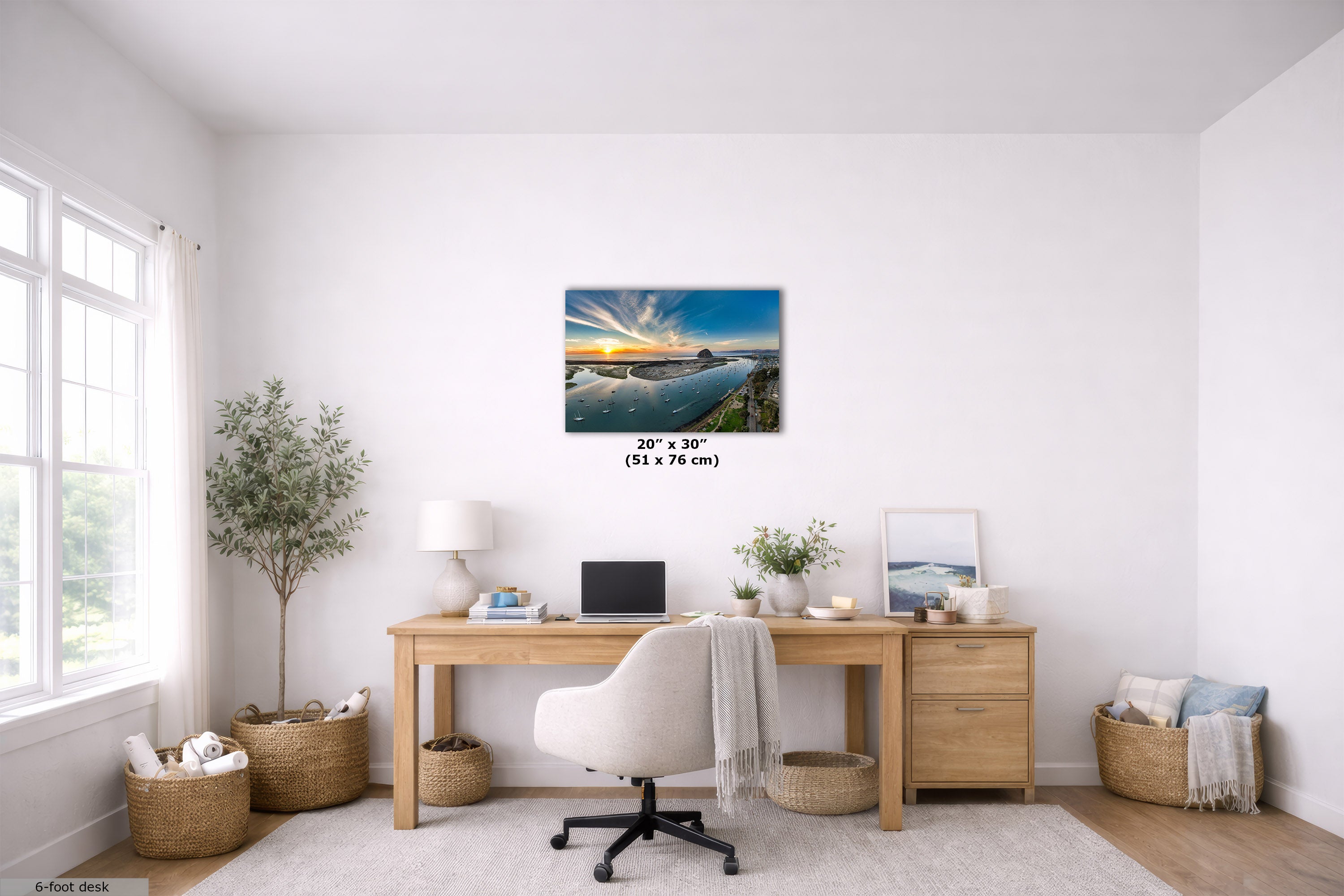 A 20" x 30" canvas print of a coastal sunset landscape is displayed on a white wall in a bright, modern home office setting with a wooden desk, white chair, and plants.