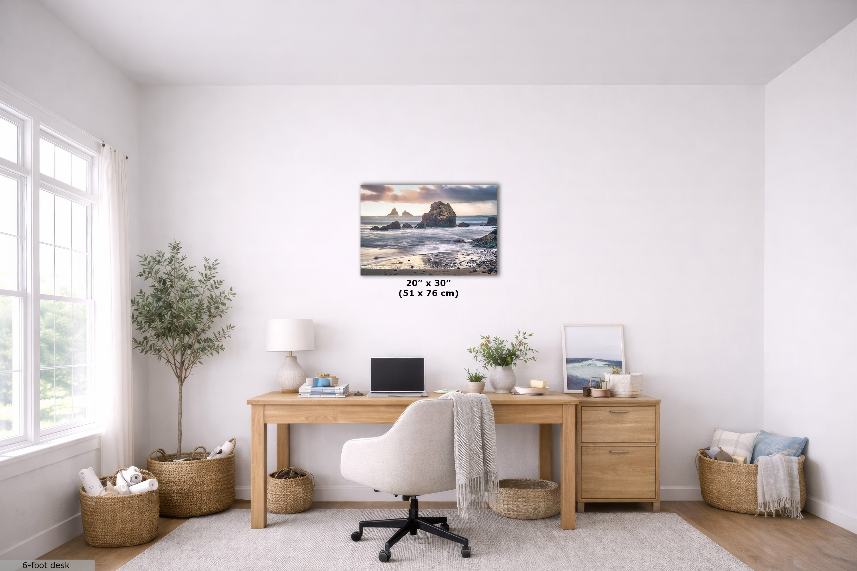 A 20" x 30" (51 cm x 76 cm) canvas print of a coastal rock formation at sunset, displayed on a white wall in a modern, bright home office setting above a wooden desk.