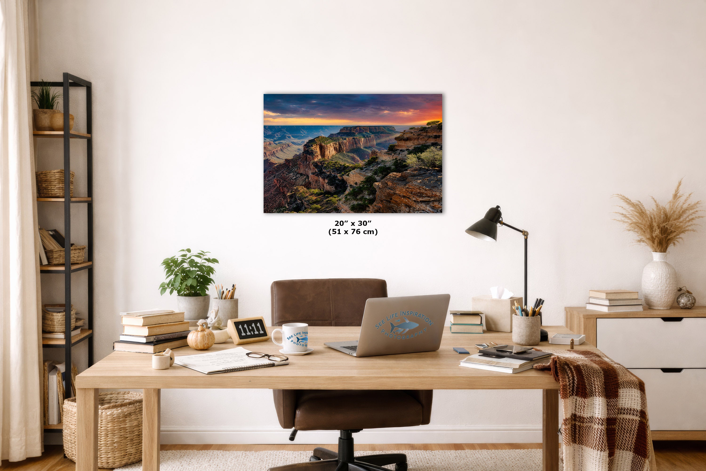 A framed wall art print depicting a colorful canyon landscape with a sunset sky, displayed above a wooden desk in a styled home office setting. The print has size text below it reading 20 x 76 inches.