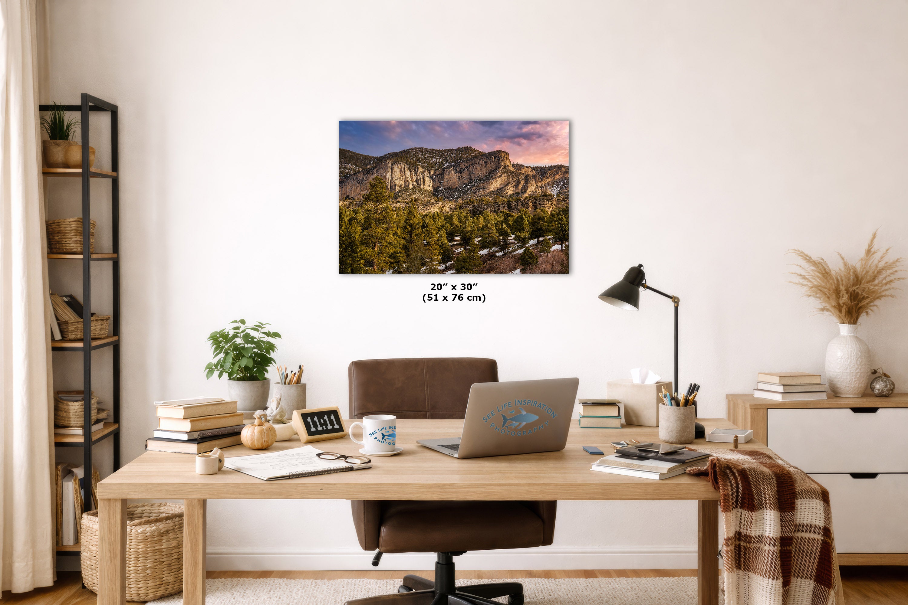 A wall art print showing a mountain landscape at sunset hangs above a wooden desk in a styled home office. The print includes size text reading 20 x 30 cm.