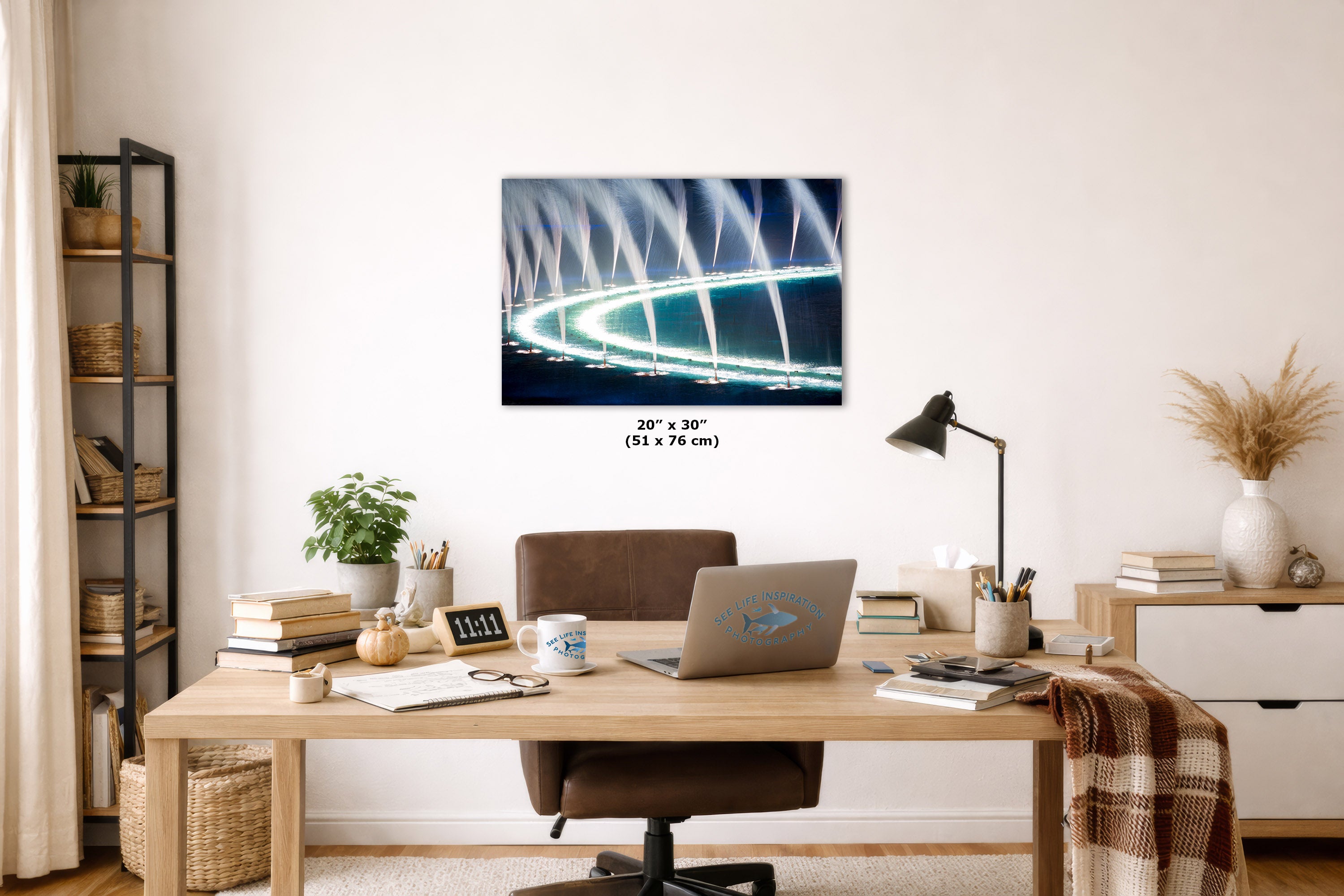 A wall art print depicting a glowing futuristic curved fountain structure at night, displayed above a wooden desk in a styled home office. The print includes size text reading 20 x 30 inches.