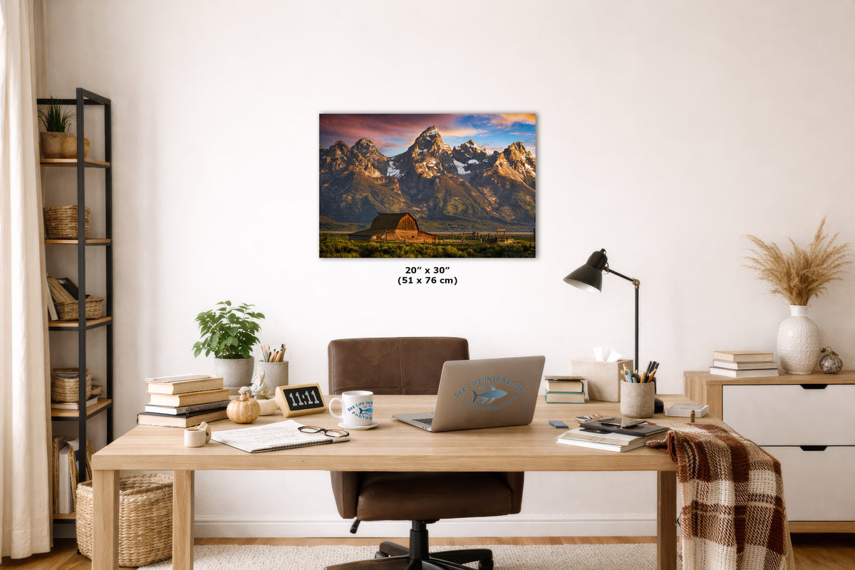 A wall art print showing the Grand Teton mountain landscape with a small cabin, displayed above a wooden desk in a styled home office. The print includes size text reading 20 x 30-inches.