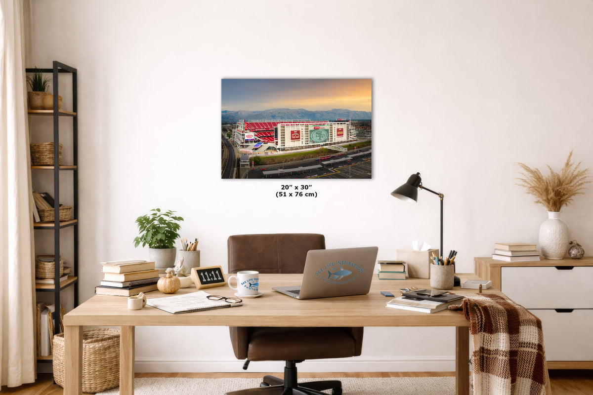 A wall art print showing a stadium at dusk is displayed above a wooden desk in a styled home office. The print includes size text reading 20 x 30 inches.